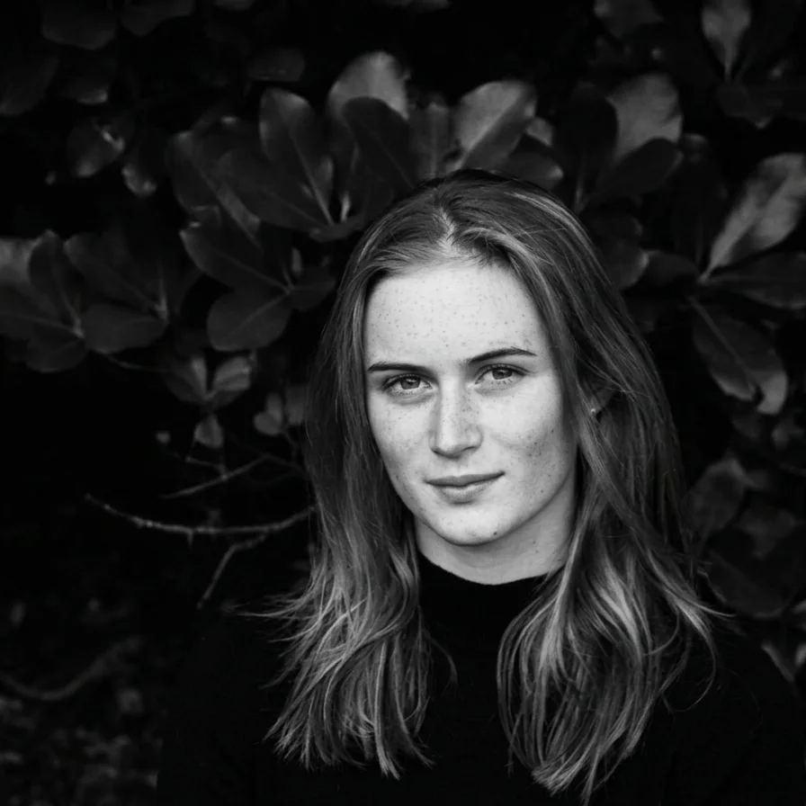 Black-and-white portrait of a freckled woman with long hair standing in front of leafy foliage