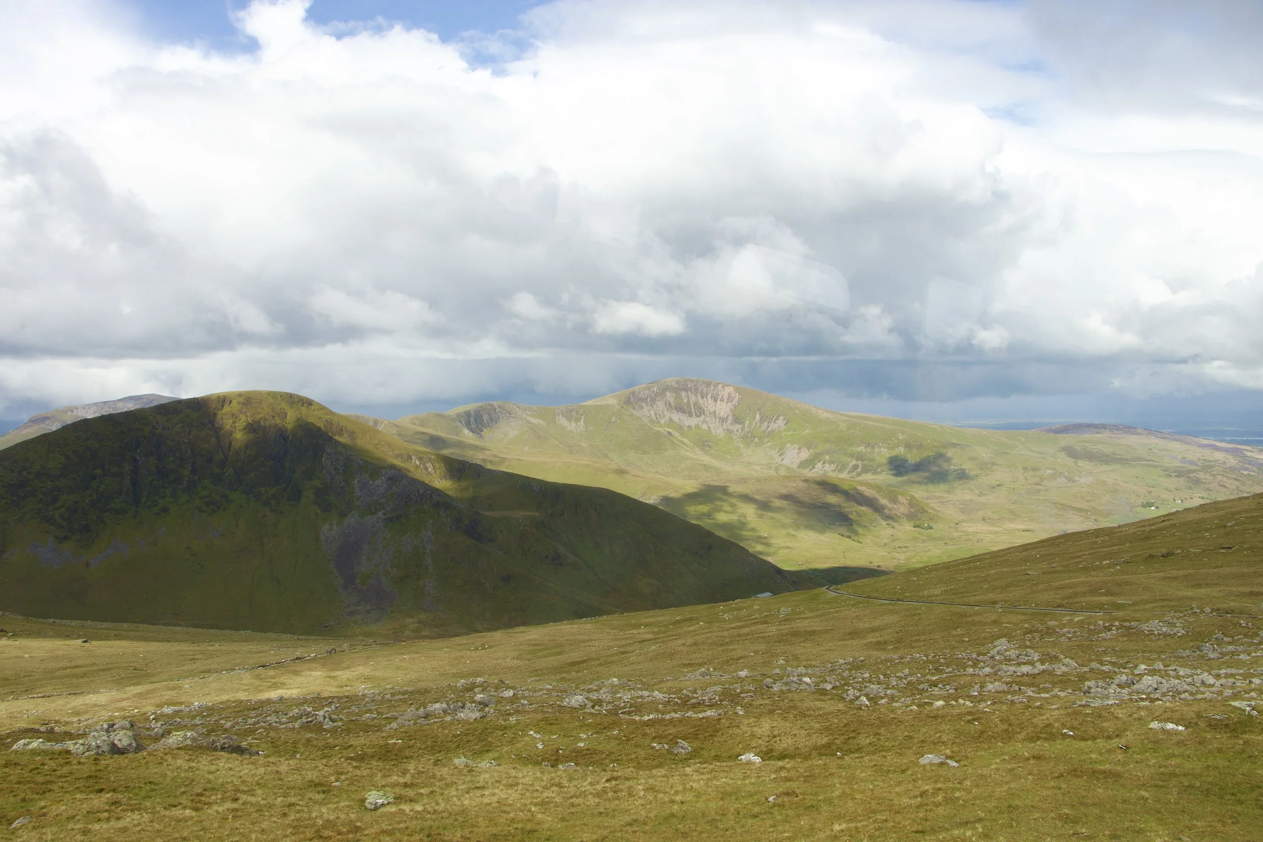 Panoramic view of green, rocky mountain hills beneath dramatic clouds.