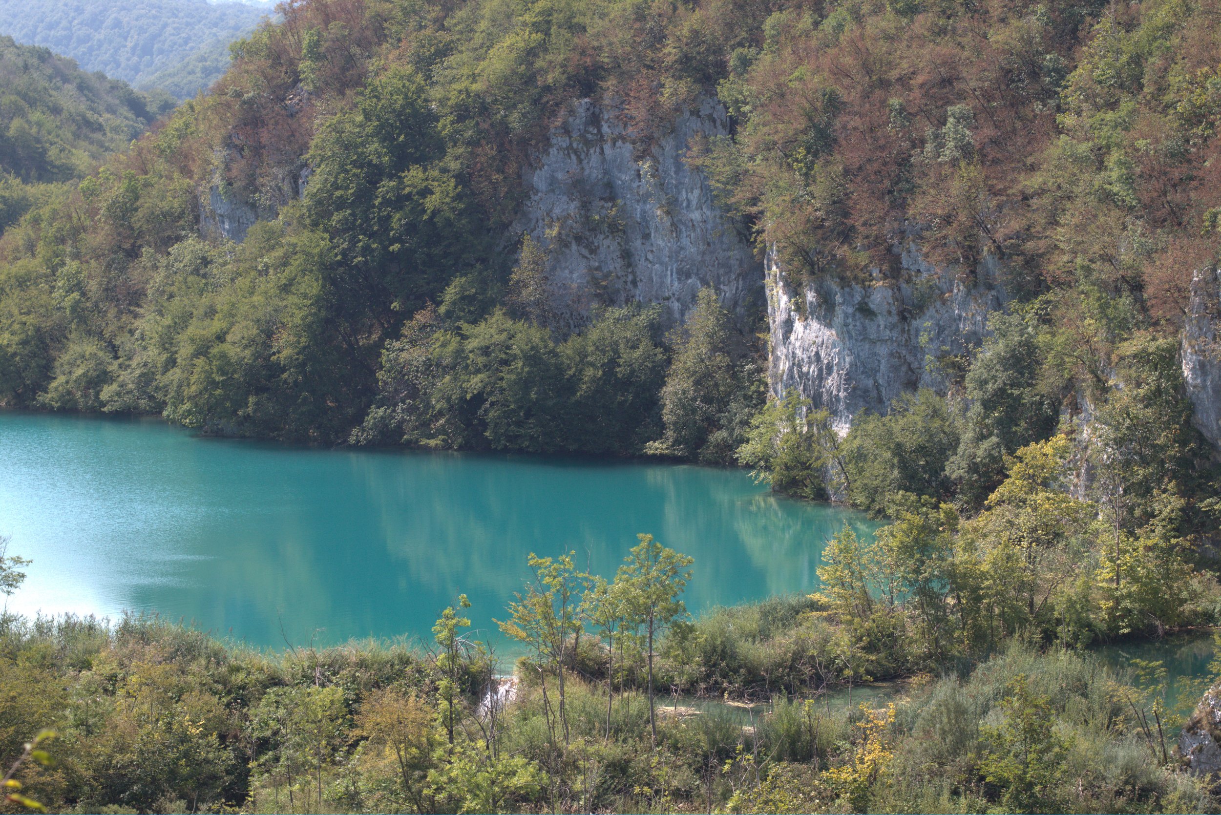 Turquoise lake surrounded by dense forest and rugged limestone cliffs in a mountainous landscape