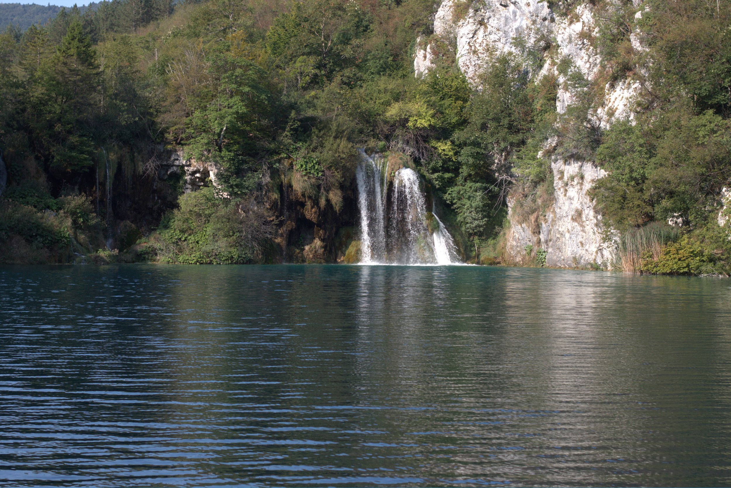 Waterfall cascading into a lake beneath forested limestone cliffs