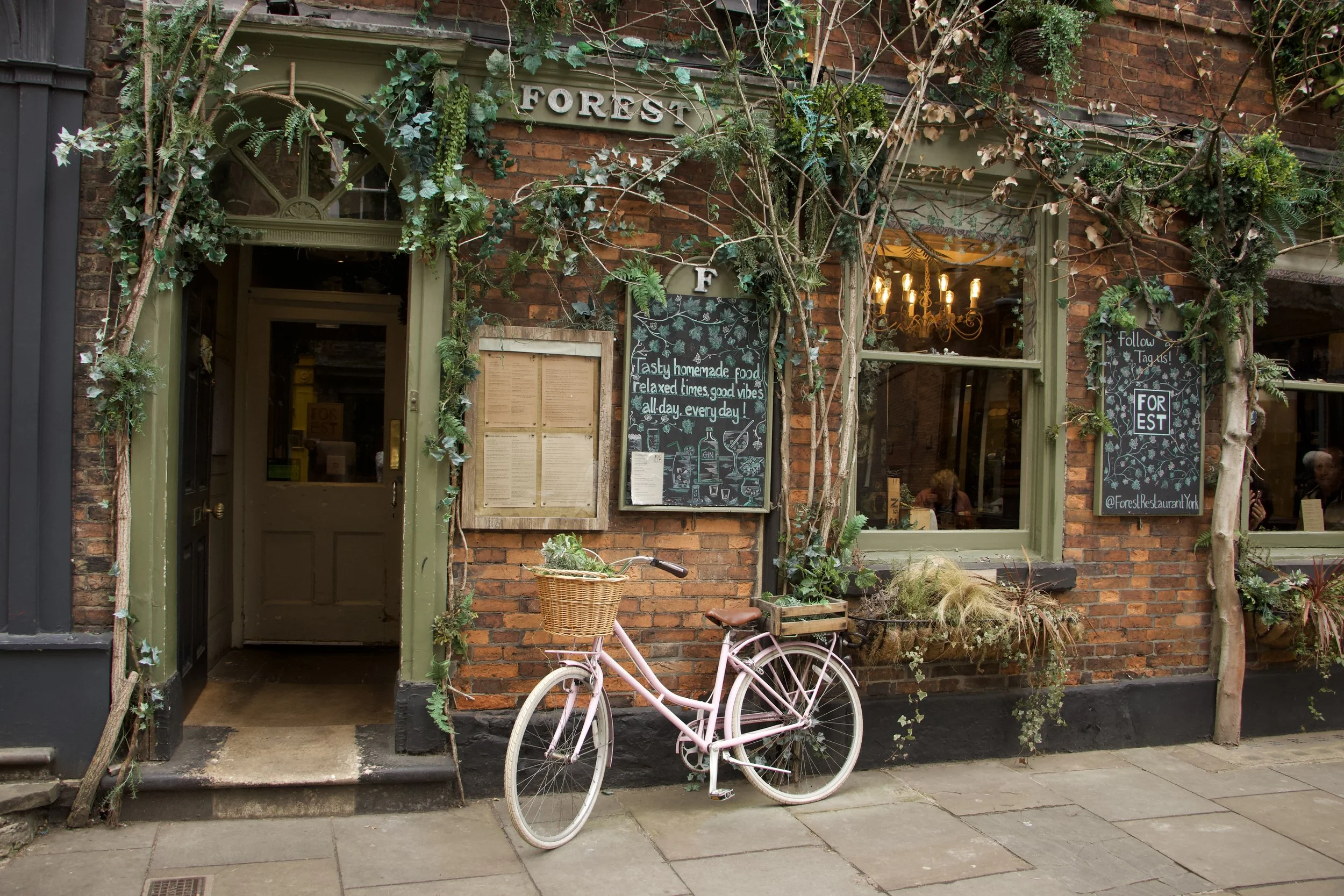 Ivy-covered Forest restaurant facade with chalkboard menus and a pink bicycle outside.