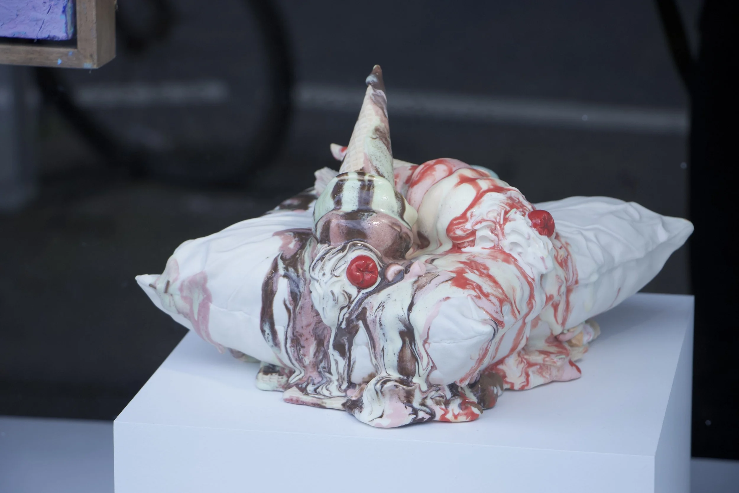 Surreal ceramic sculpture of melting ice cream and a cone on a white pedestal.
