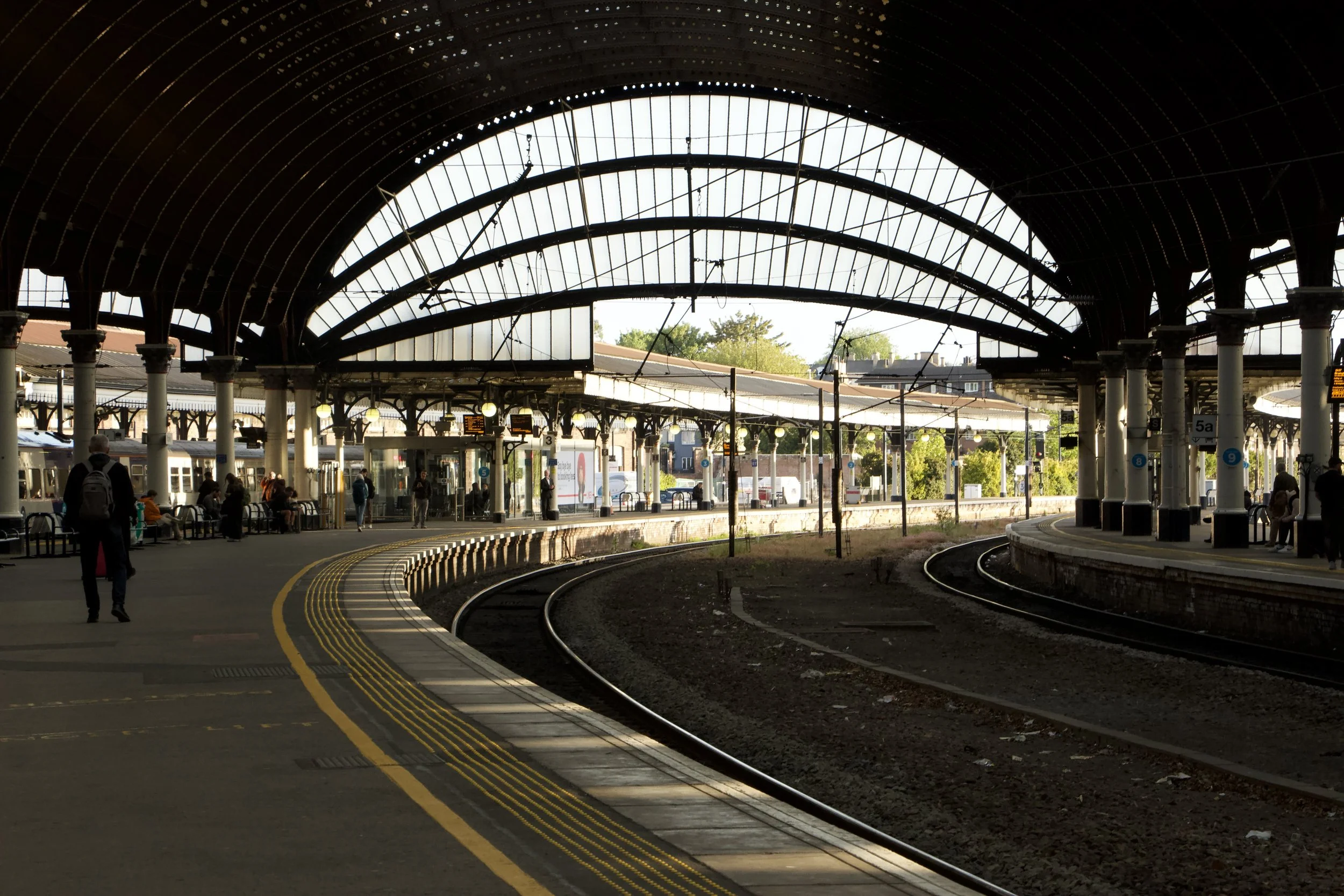 York's covered railway station with arched glass roof, curved train tracks, platforms, and waiting passengers.