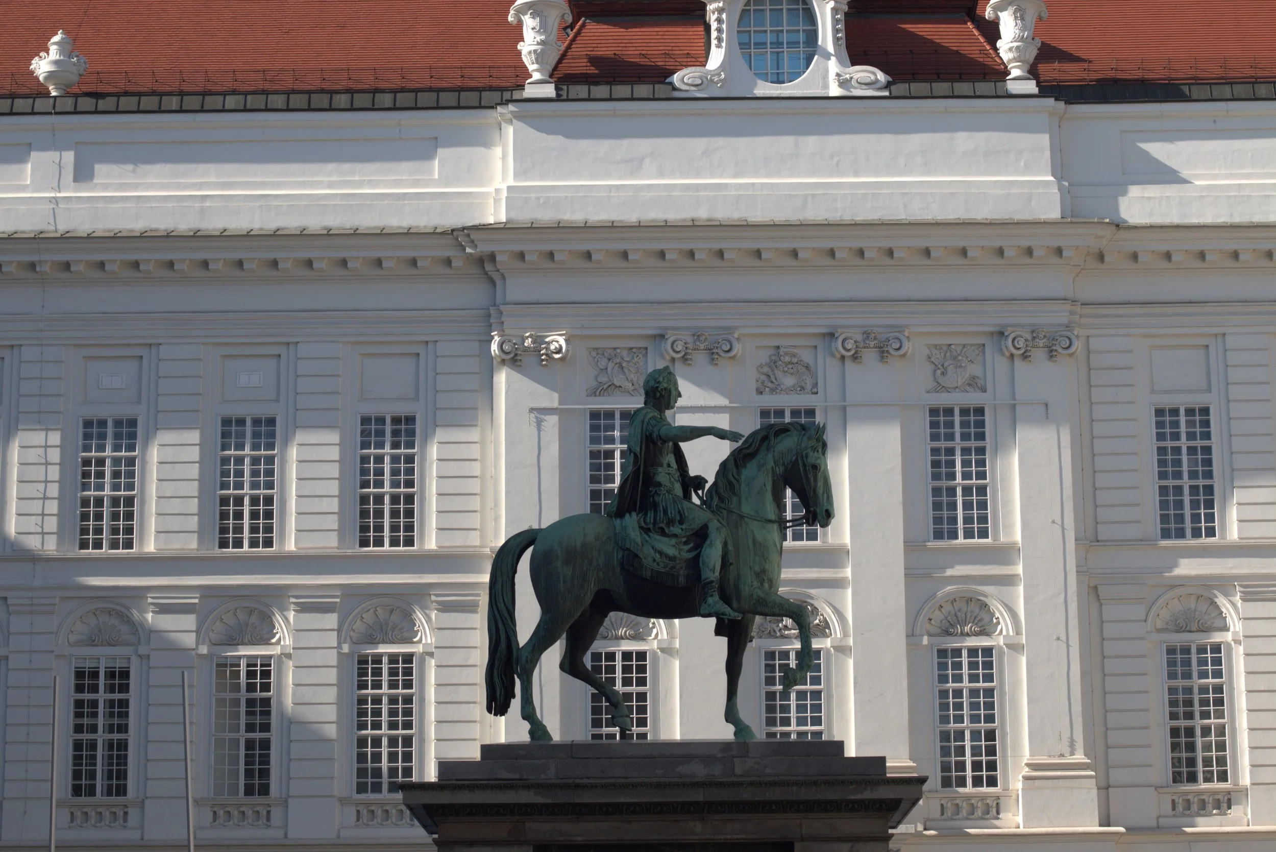 Bronze equestrian statue in front of an ornate white neoclassical building with a red tile roof