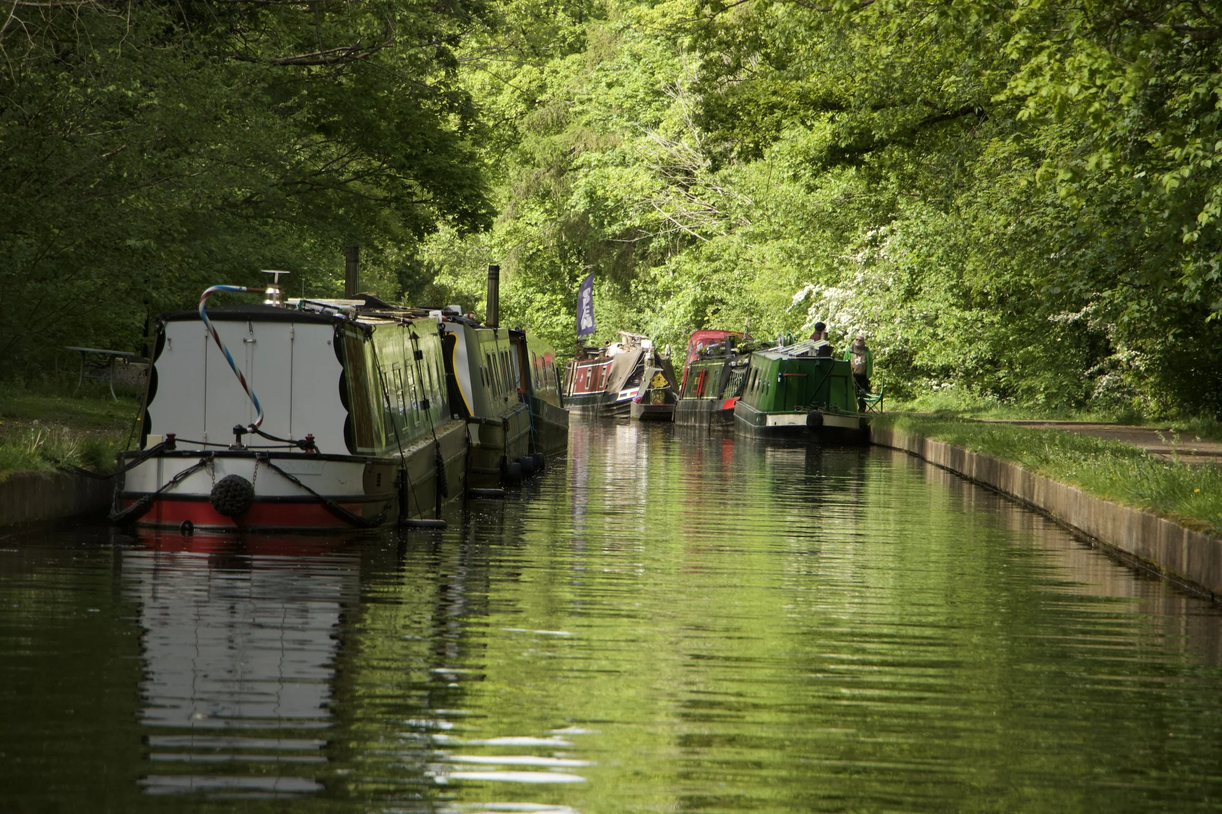 Colorful narrowboats moored along a lush, tree-lined Pontcysyllte Canal with reflections in the calm water.