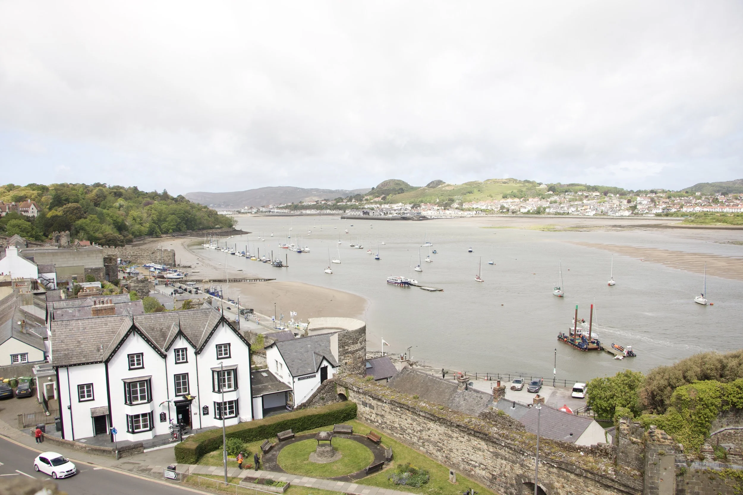 Panoramic view of Conwy, Wales, showing the tidal estuary, sailboats, historic town, and surrounding hills.