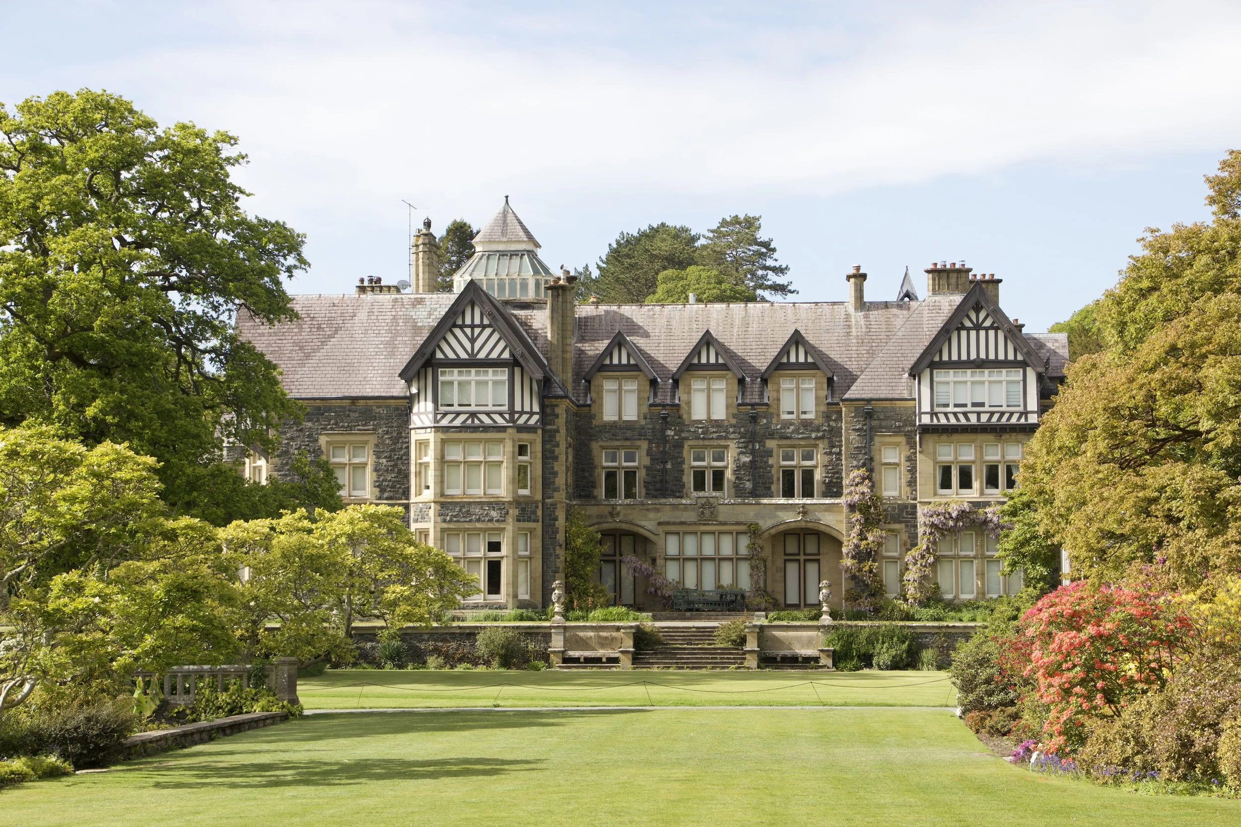 Historic Tudor-style stone mansion surrounded by landscaped gardens and a manicured lawn in Bodnant Garden.