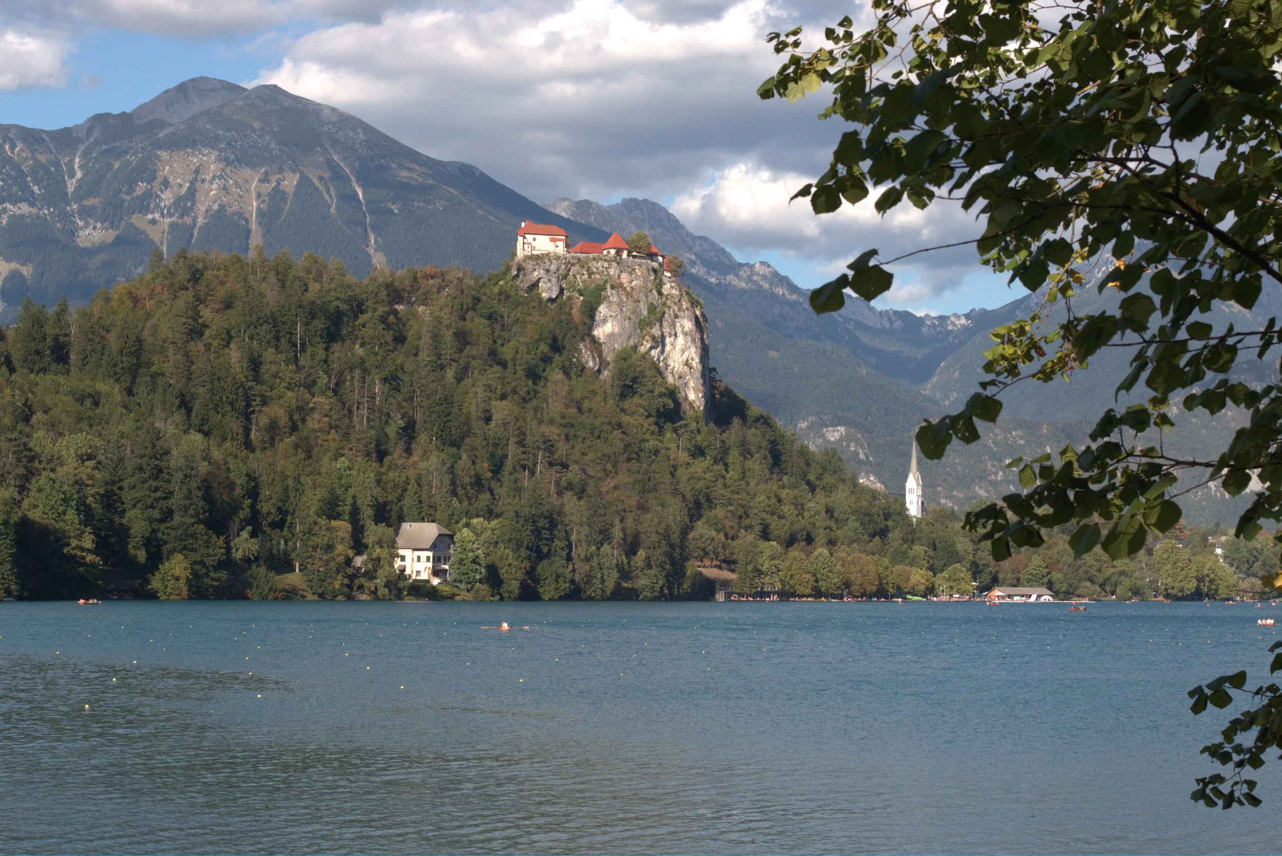 Scenic view of Lake Bled in Slovenia with Bled Castle on a rocky cliff, alpine mountains, forest, and a lakeside church