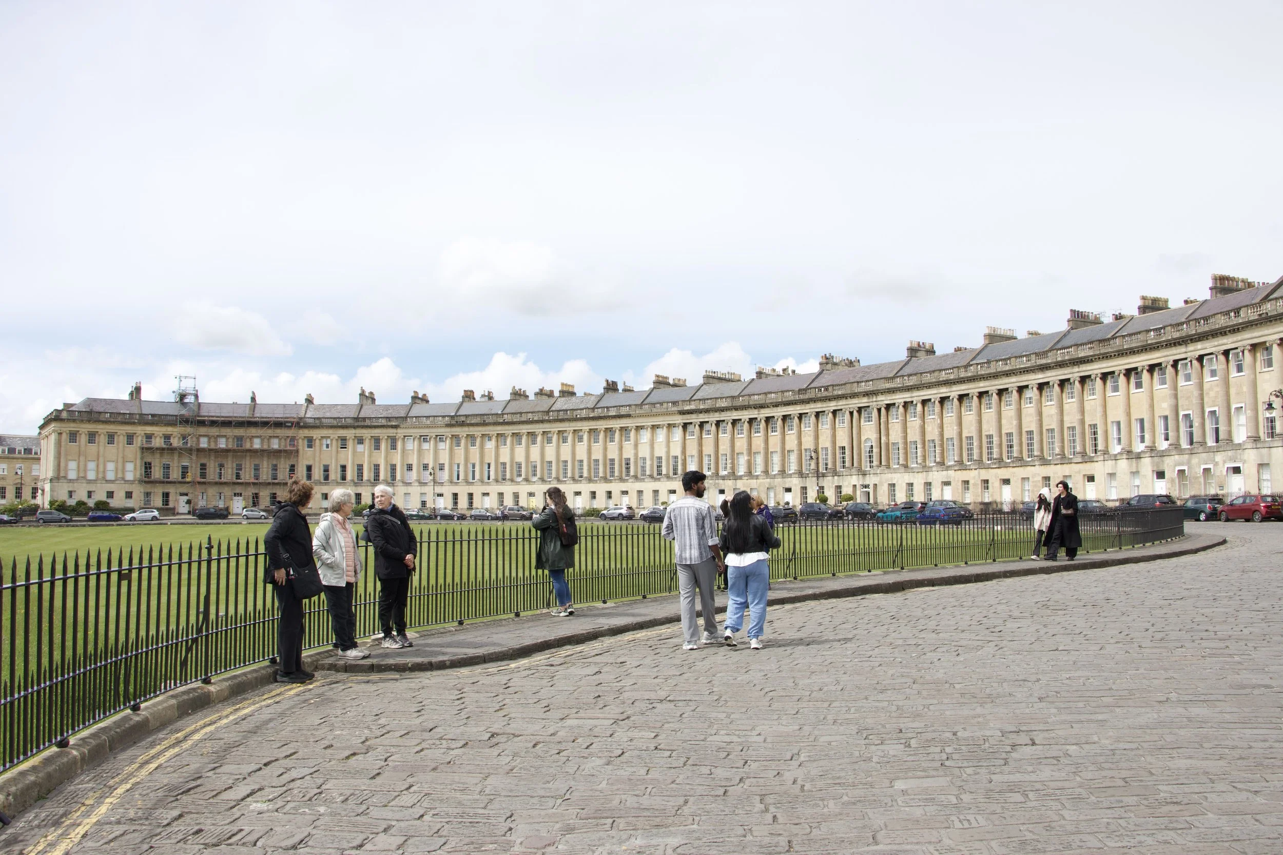 Tourists beside a wrought-iron fence overlooking the Royal Crescent’s Georgian buildings in Bath, England.