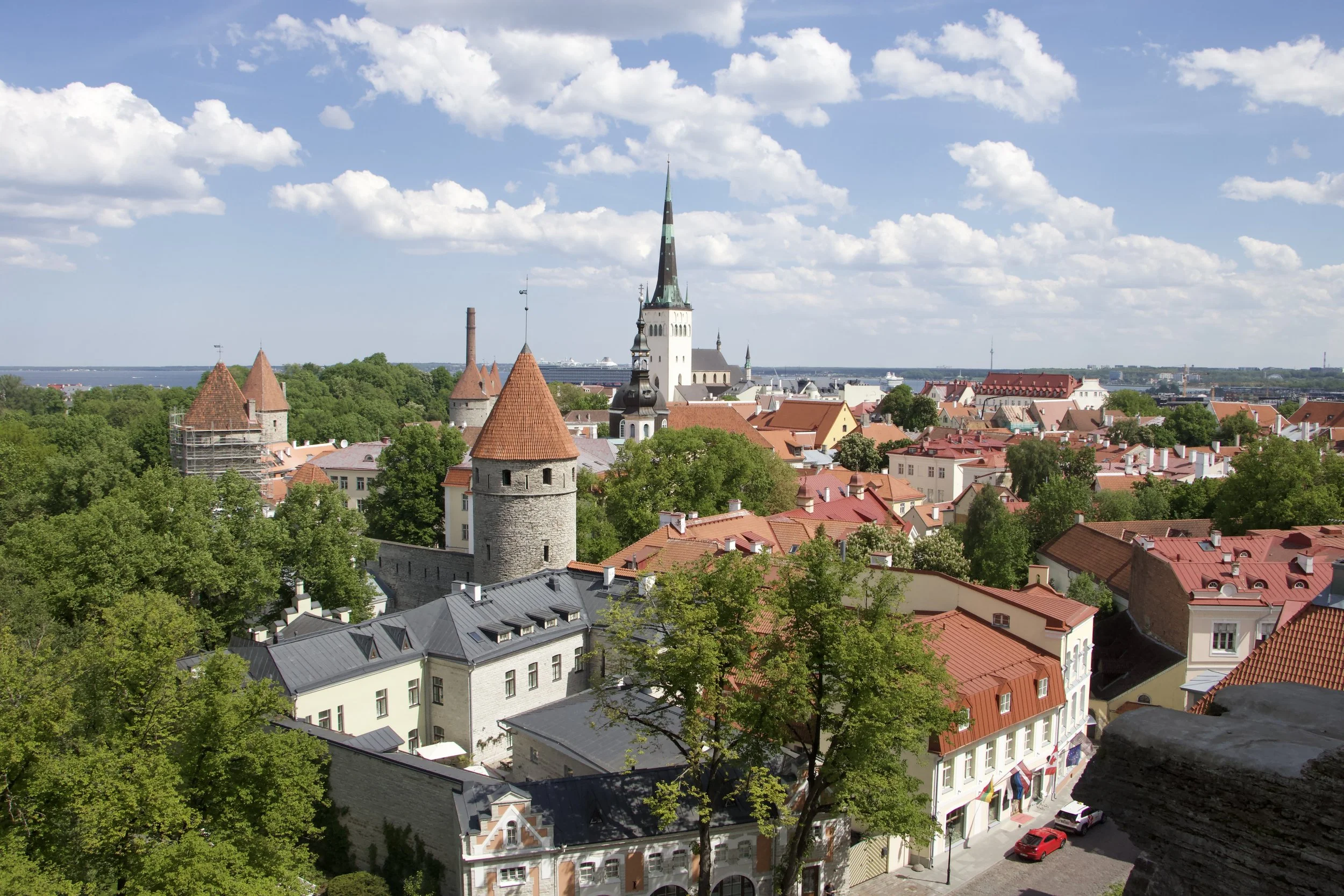 Panoramic view of Tallinn, Estonia, featuring medieval red-roofed buildings, stone towers, St. Olaf’s Church, and the Baltic Sea.