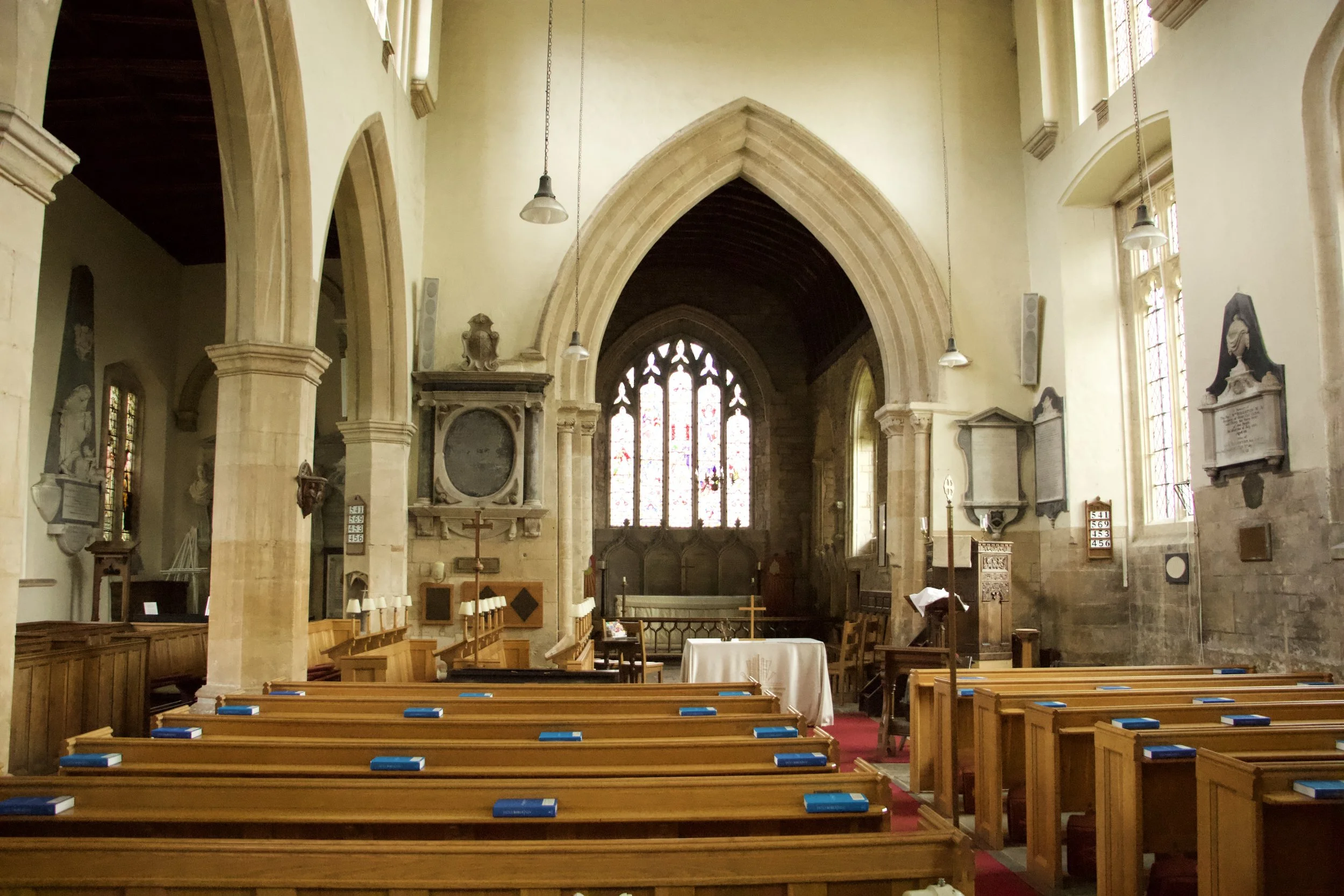 Interior of a Blockley's history church with Gothic arches, stained-glass windows, wooden pews, memorial plaques, and a central altar.
