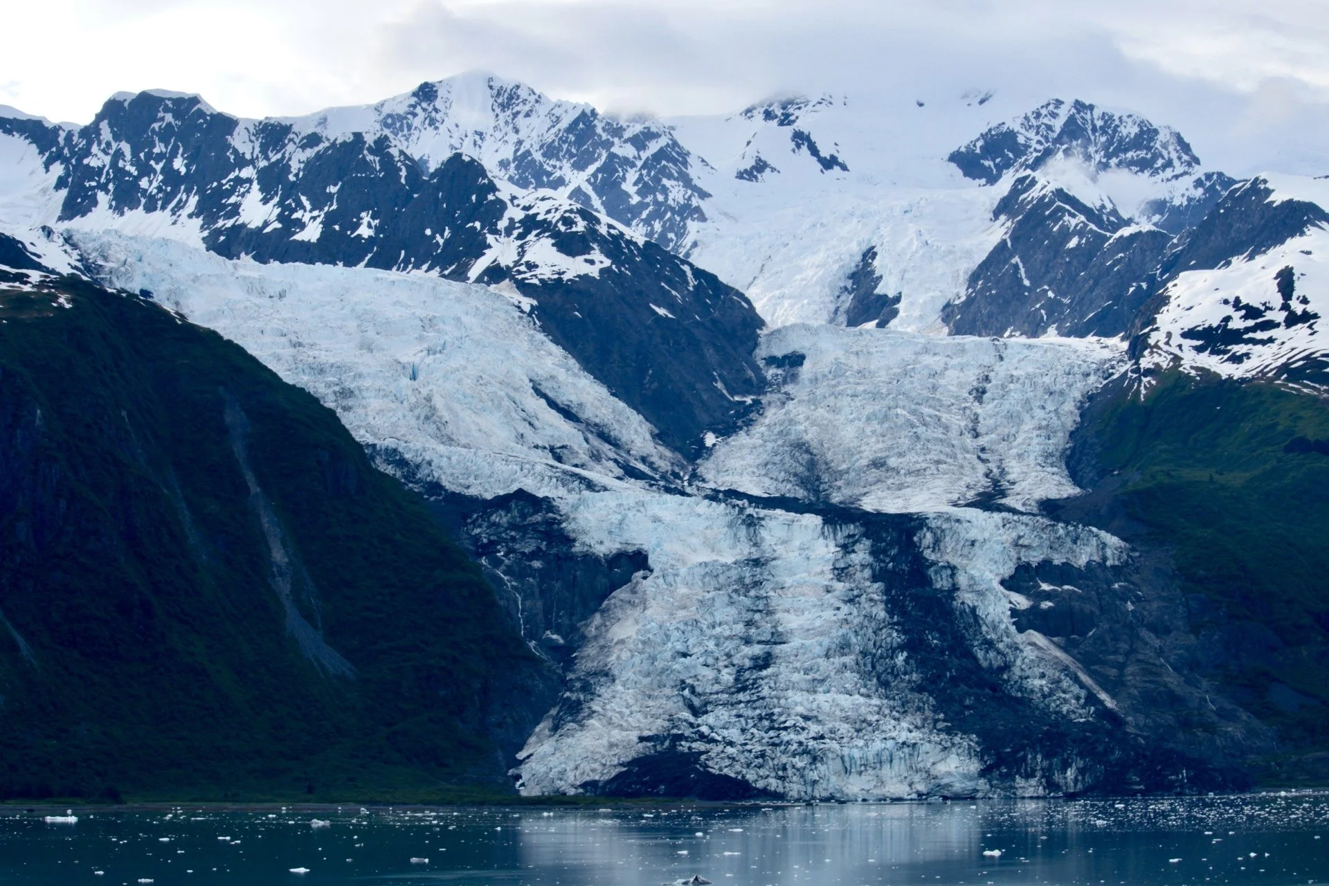 Snow-covered mountains and a massive glacier flowing into a calm fjord with floating ice.