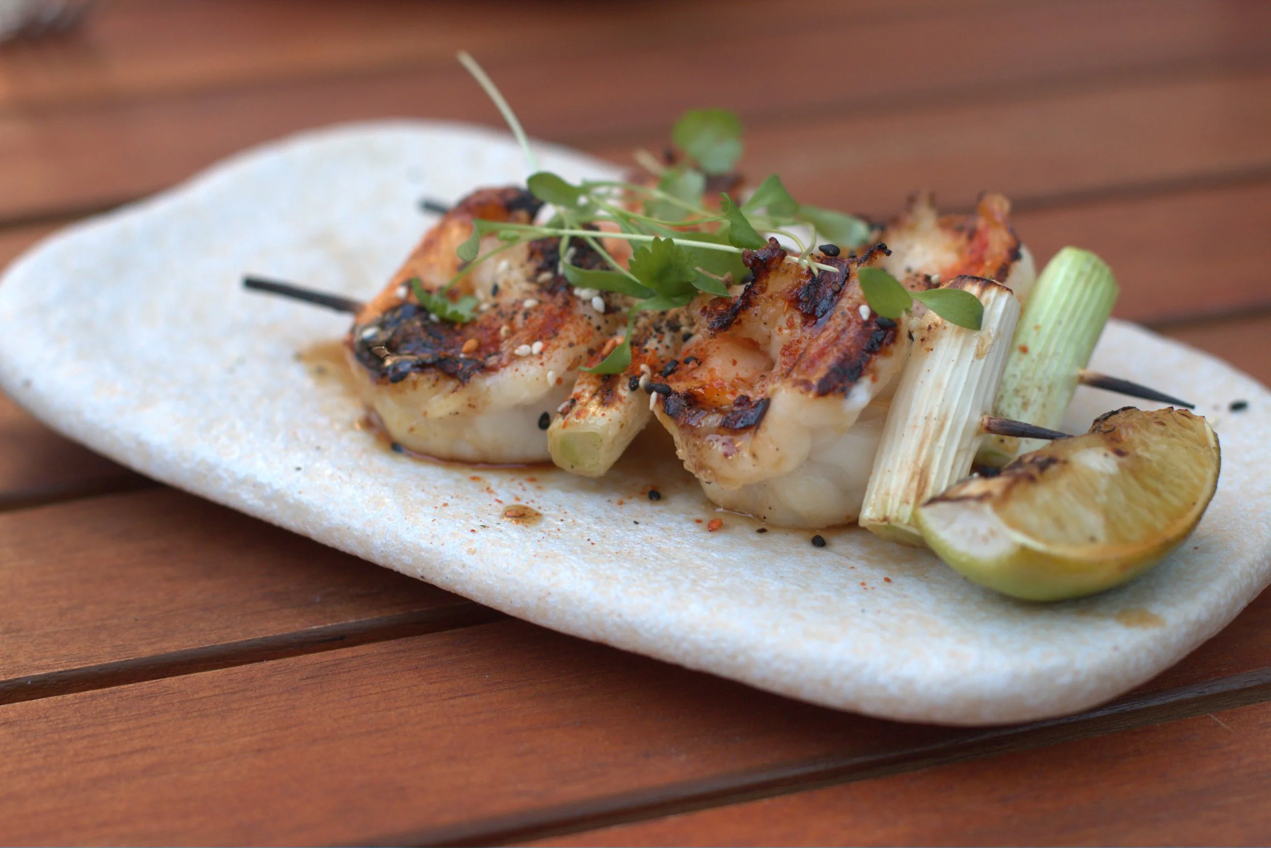 Grilled scallops and vegetables garnished with microgreens and sesame seeds on a white plate