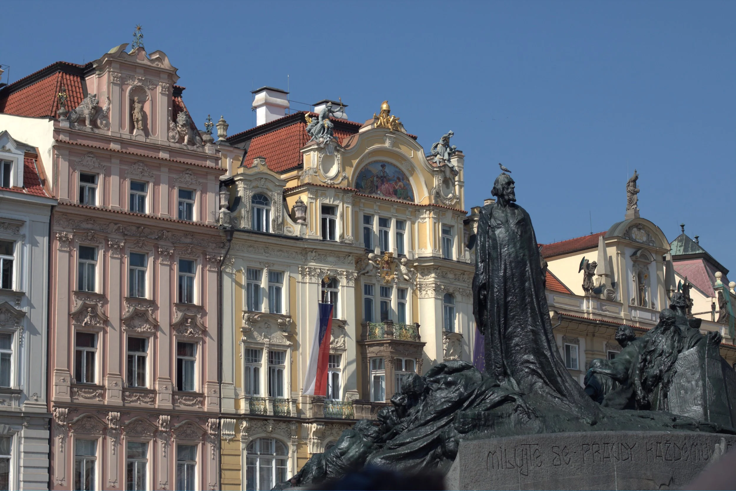 Jan Hus Memorial in Prague’s Old Town Square, with ornate Baroque buildings and colorful historic facades under a clear blue sky
