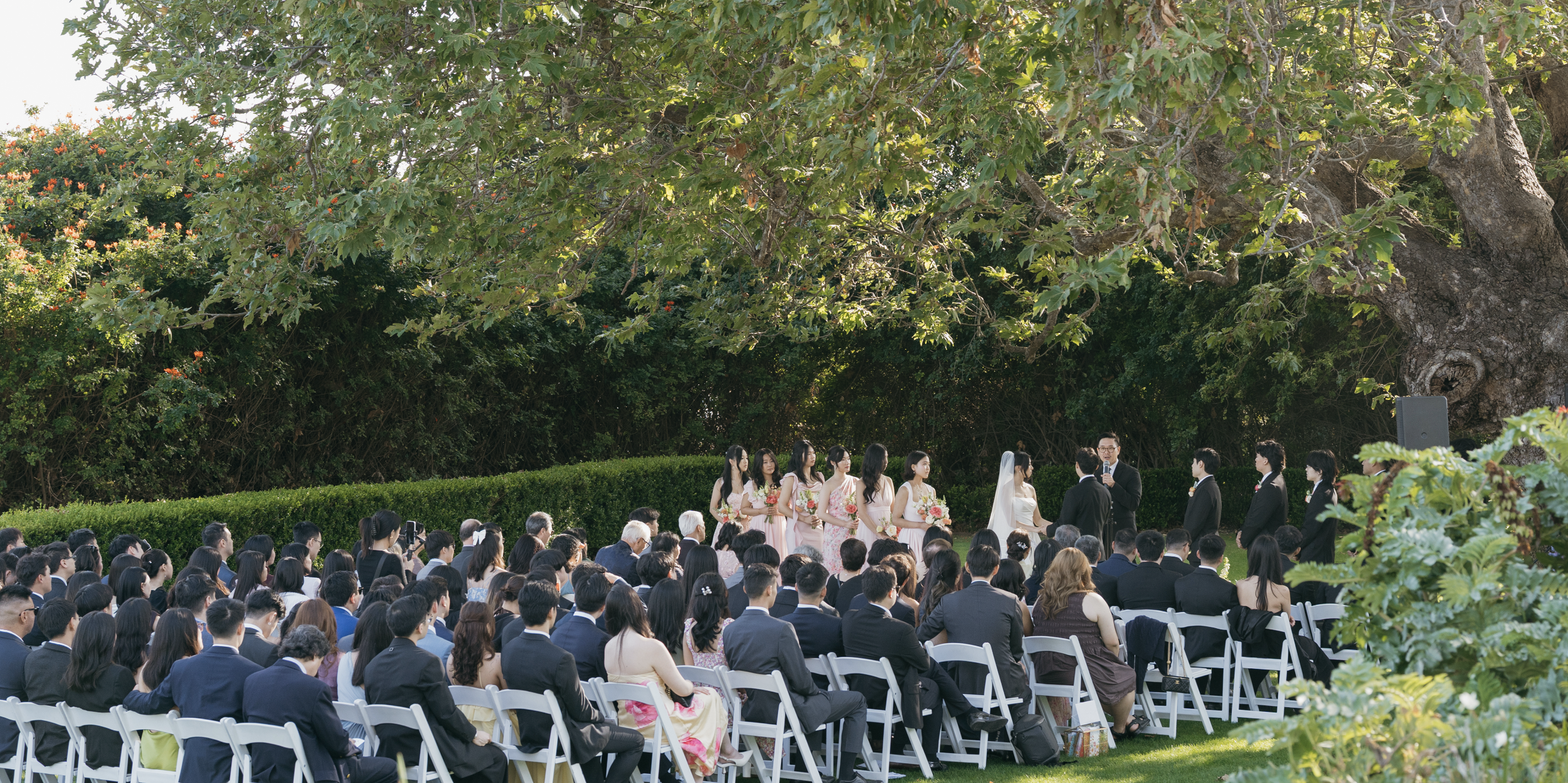 Outdoor wedding ceremony in a garden with the bride, groom, wedding party, officiant, and seated guests