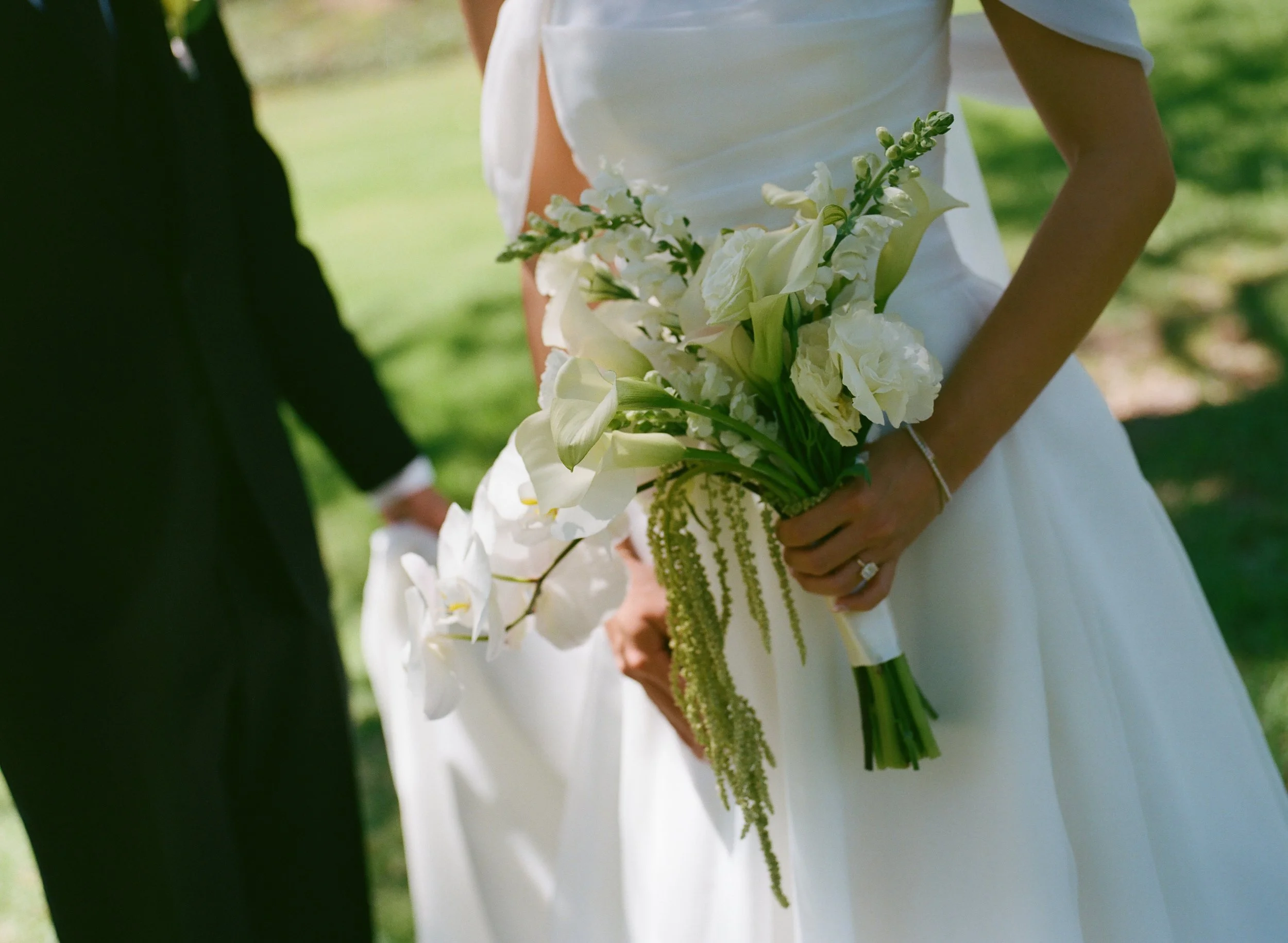 Bride in a white wedding dress holding a white floral bouquet outdoors