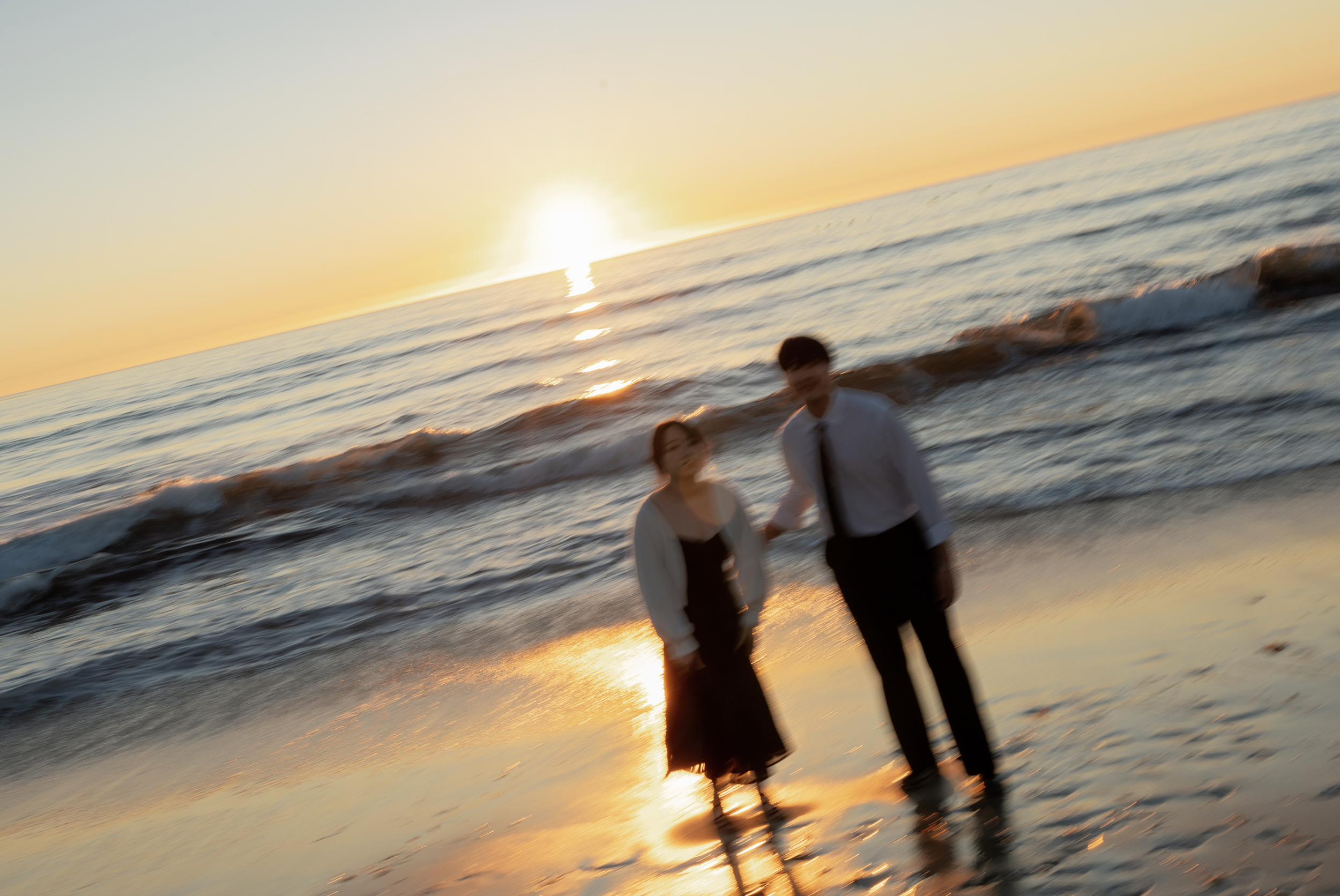 Blurred couple walking hand in hand along a beach at sunset with waves in the background