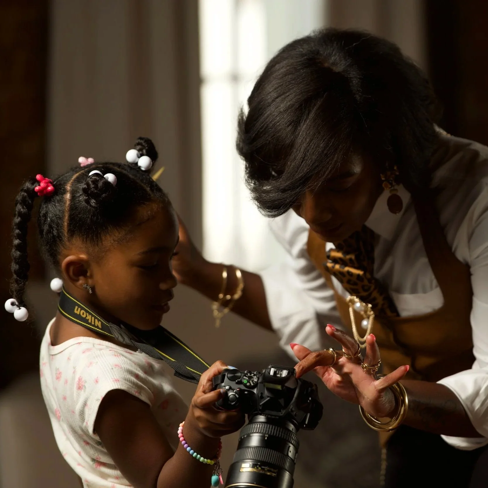 Young girl holding a DSLR camera while an adult woman helps guide her hands.