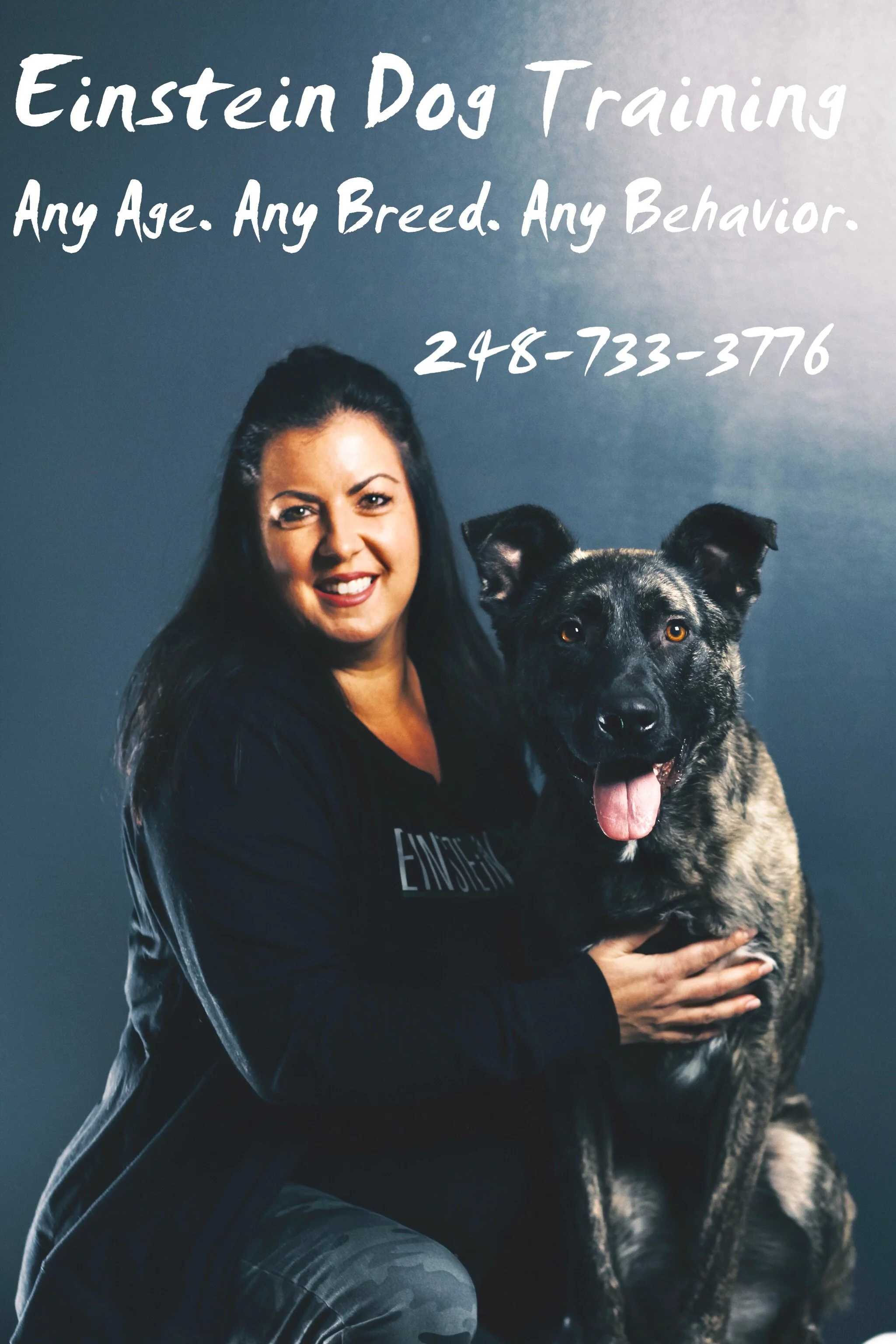Dog trainer holding a happy black and gray dog beside a sign reading “Einstein Dog Training: Any Age. Any Breed. Any Behavior.”