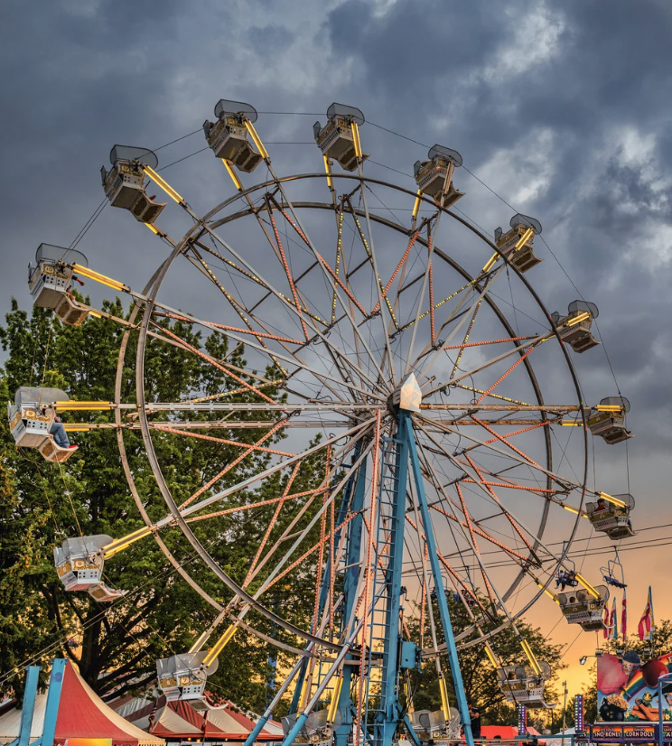 Ferris wheel with gondola seats at a carnival beneath dramatic storm clouds