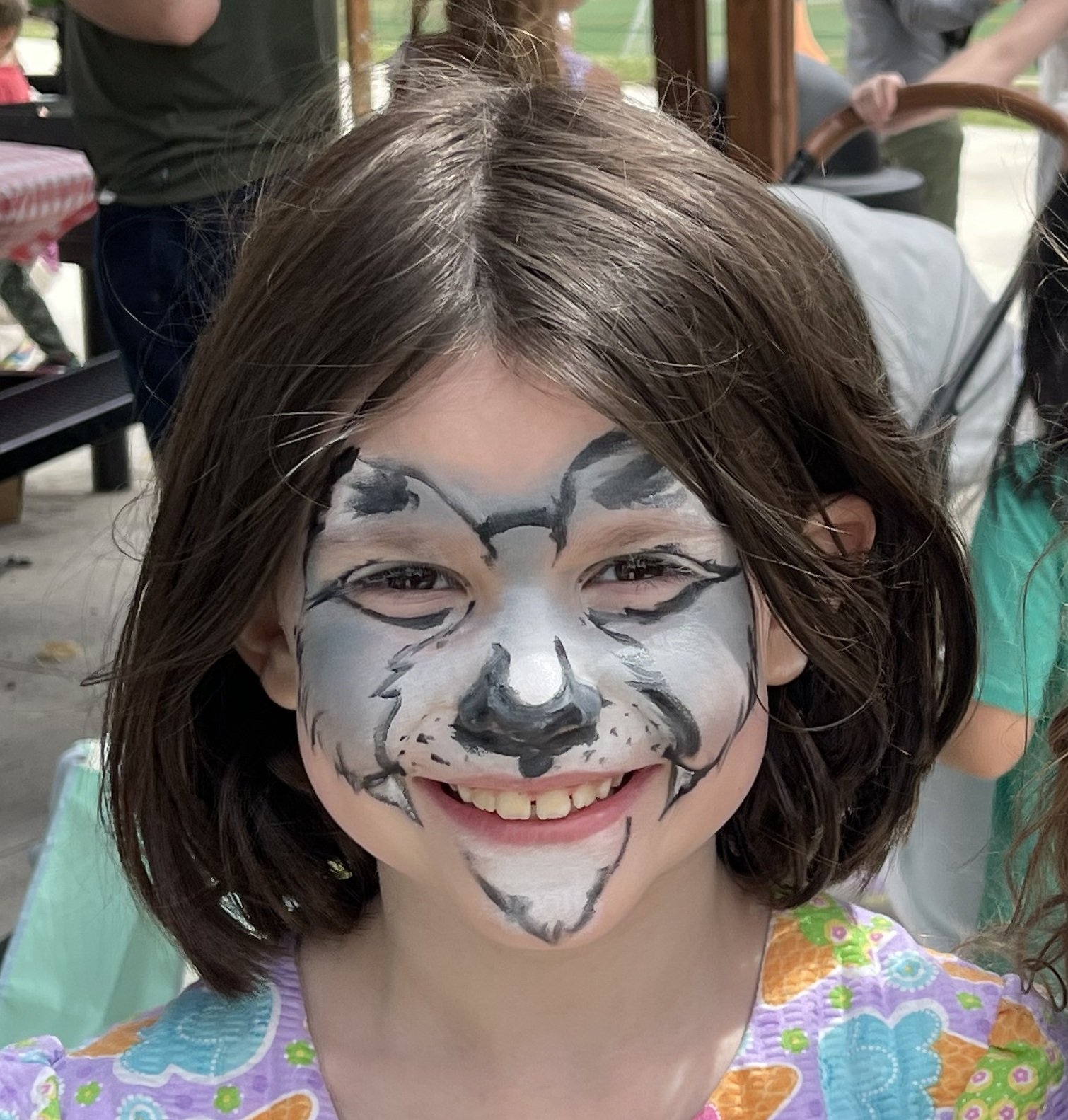 Smiling child with cat face paint and colorful floral clothing