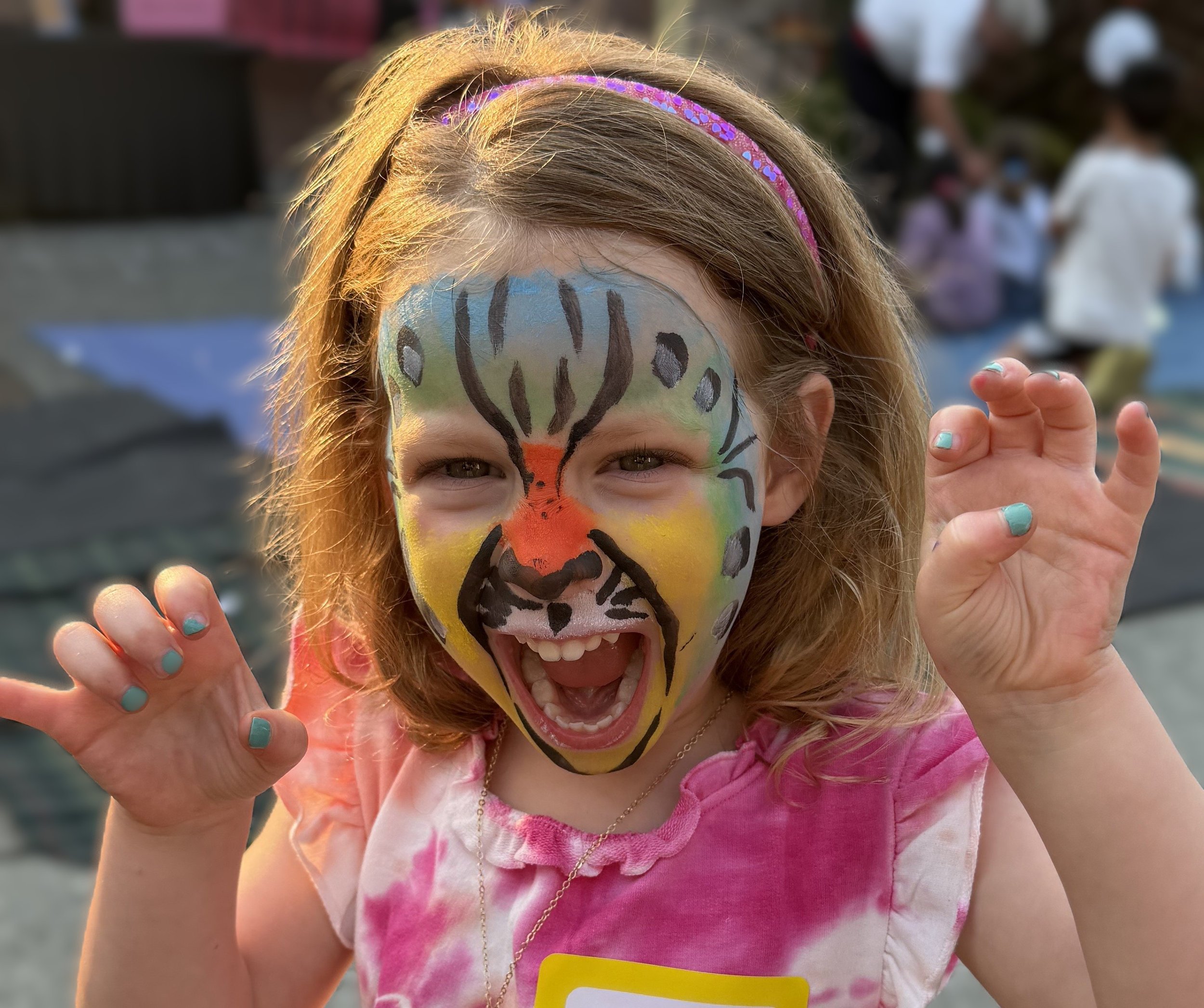 Smiling child with colorful tiger face paint posing with raised hands outdoors