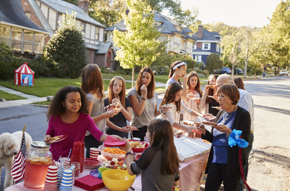 Neighbors and children enjoy a community street party with patriotic decorations, food, and drinks.