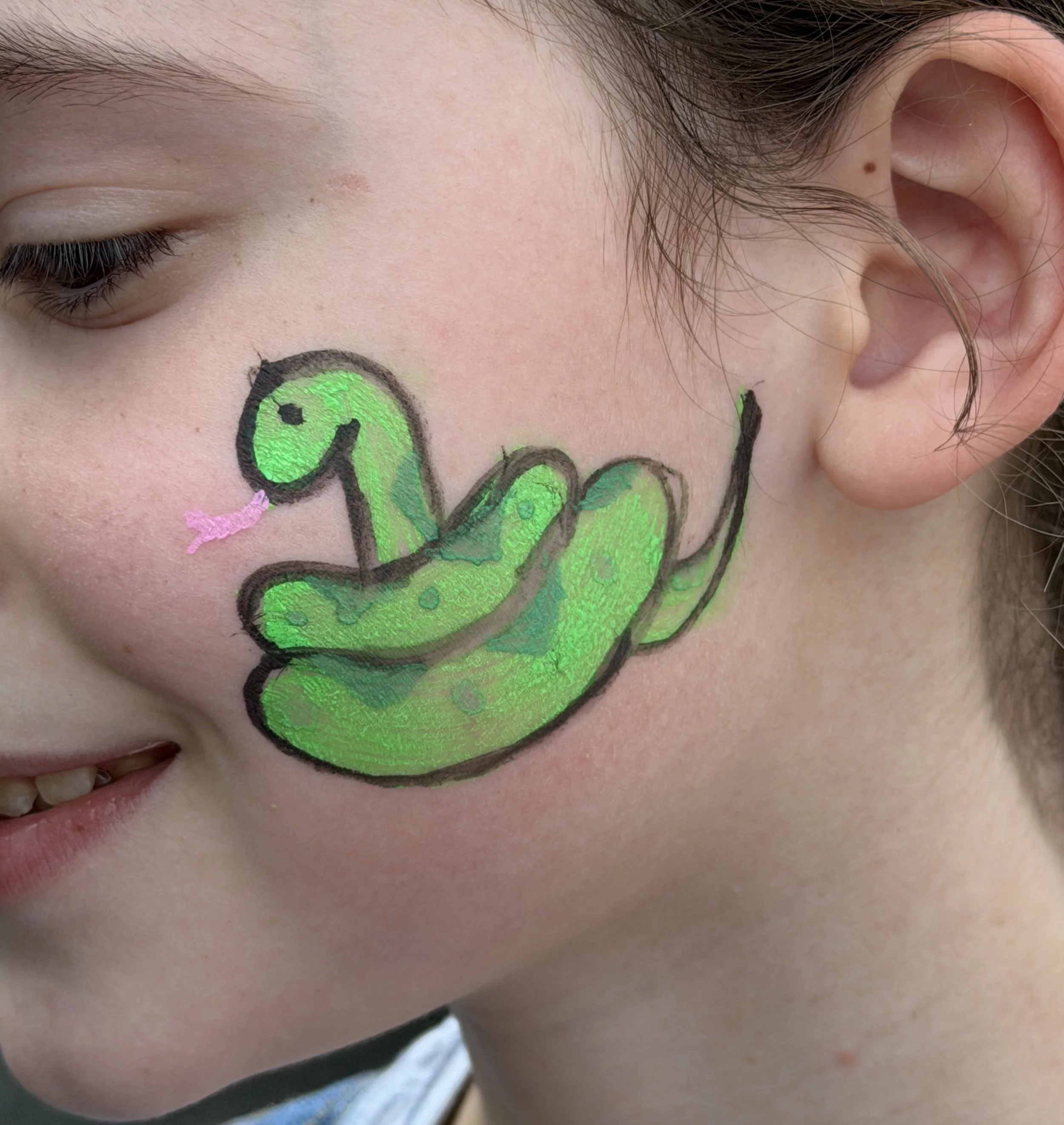 Close-up of a person with closed eyes and a bright green butterfly face-paint design on the cheek.