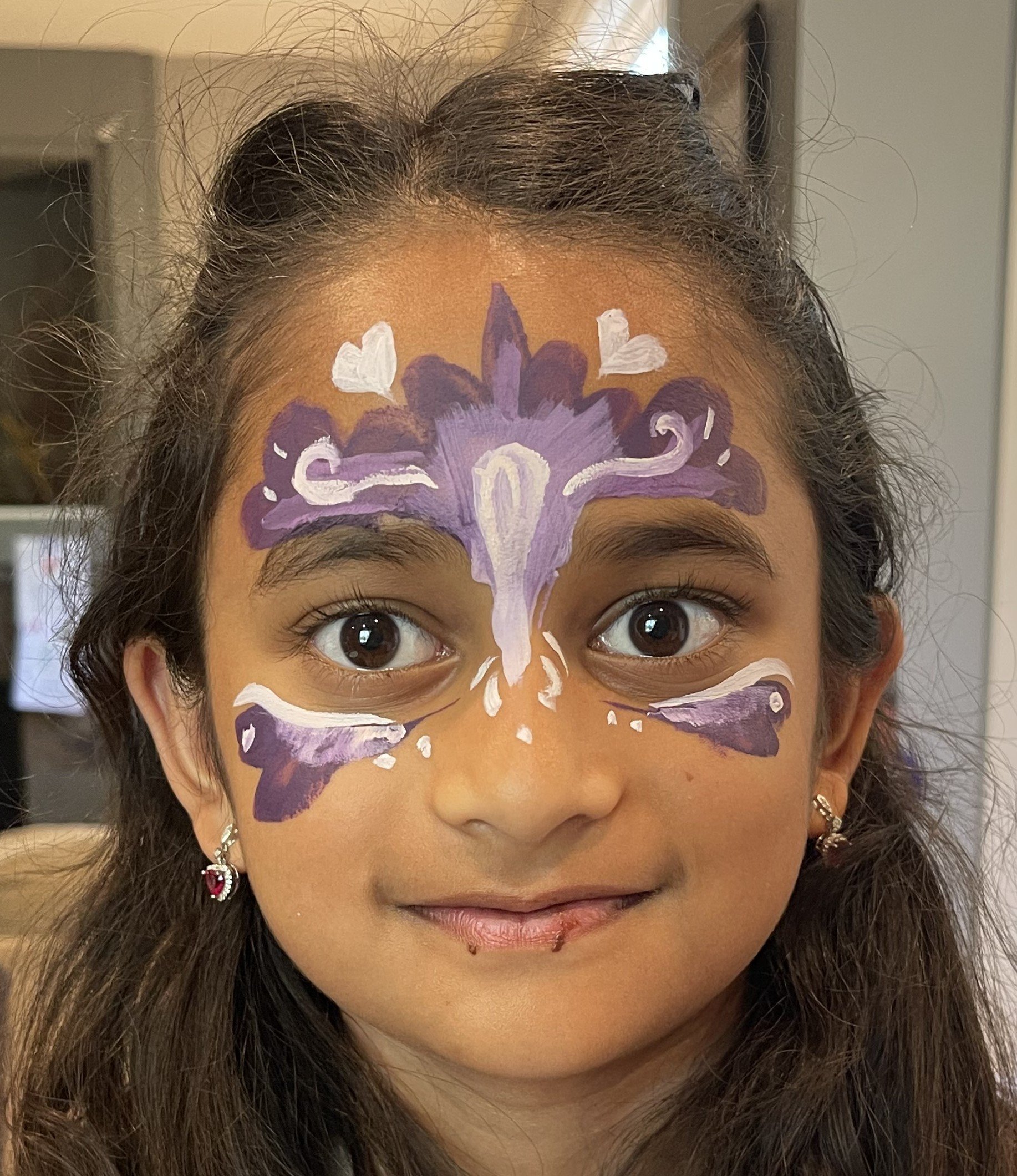 Close-up portrait of a woman wearing purple and white floral face paint.