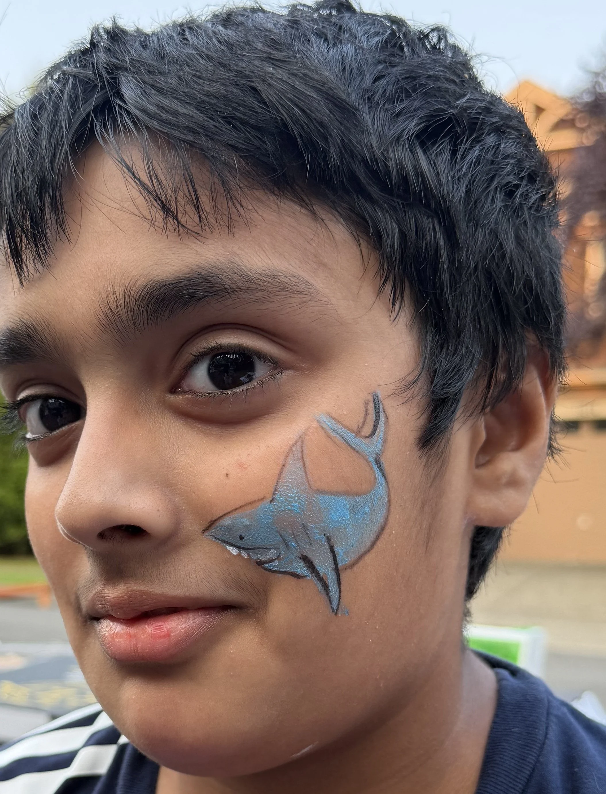 Close-up portrait of a child with short dark hair and blue butterfly face paint on one cheek.