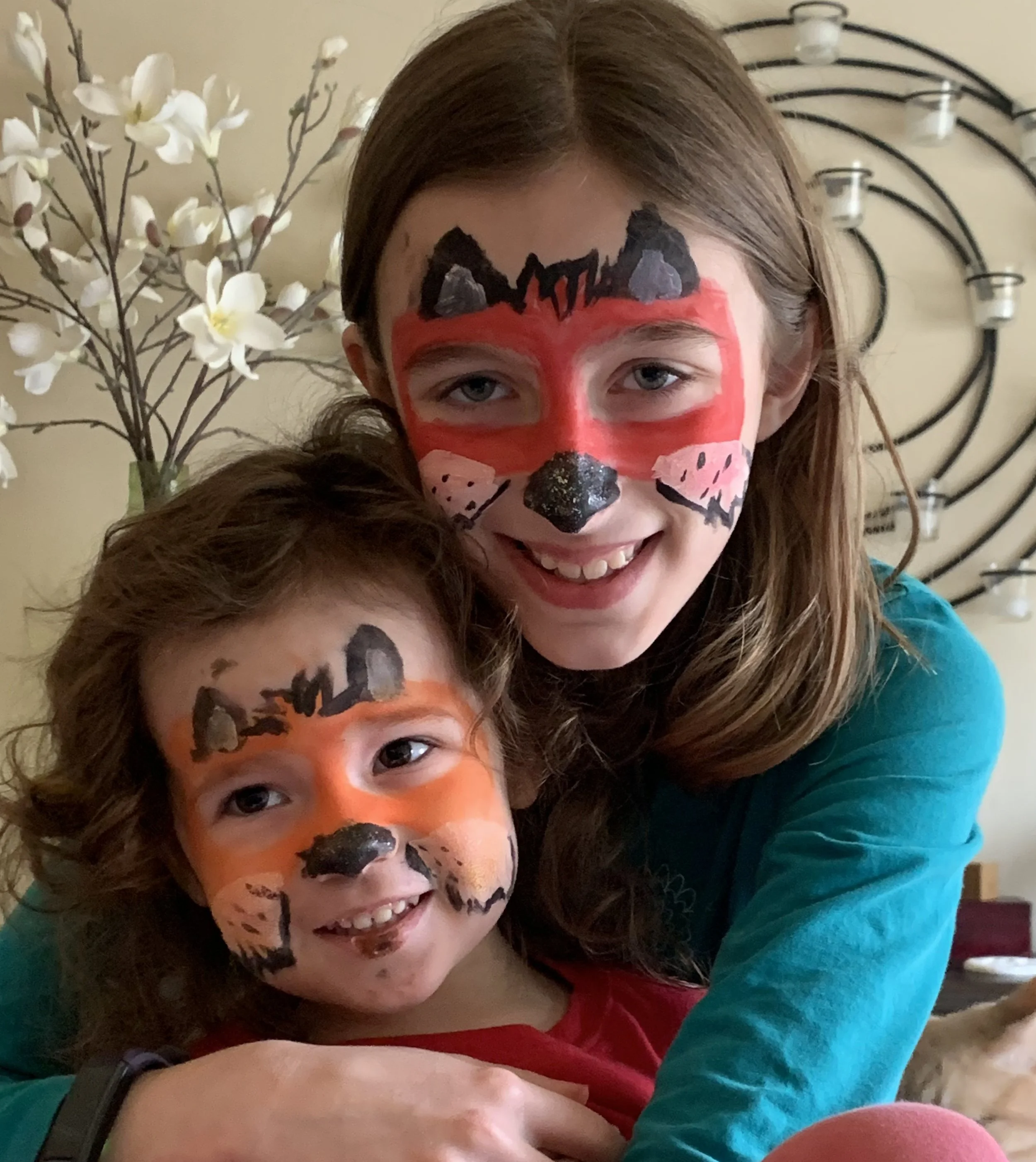 Smiling mother and child wearing colorful cat face paint in a home selfie
