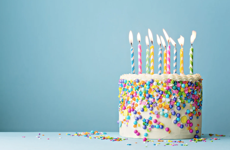Colorful birthday cake covered in sprinkles and candy decorations with striped candles against a blue background