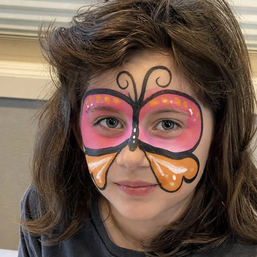 Close-up portrait of a child wearing colorful butterfly face paint in pink, orange, and black