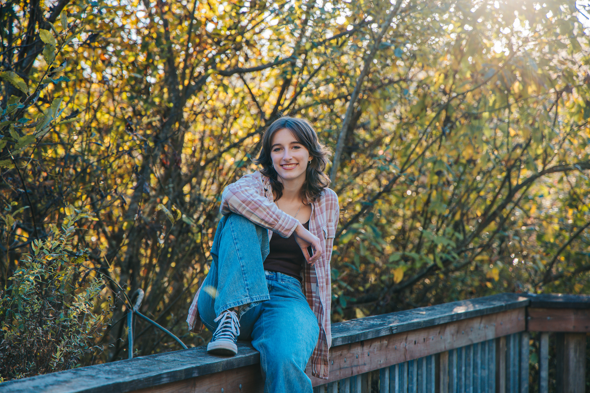 Smiling young woman sitting on a wooden bridge railing in an autumn forest