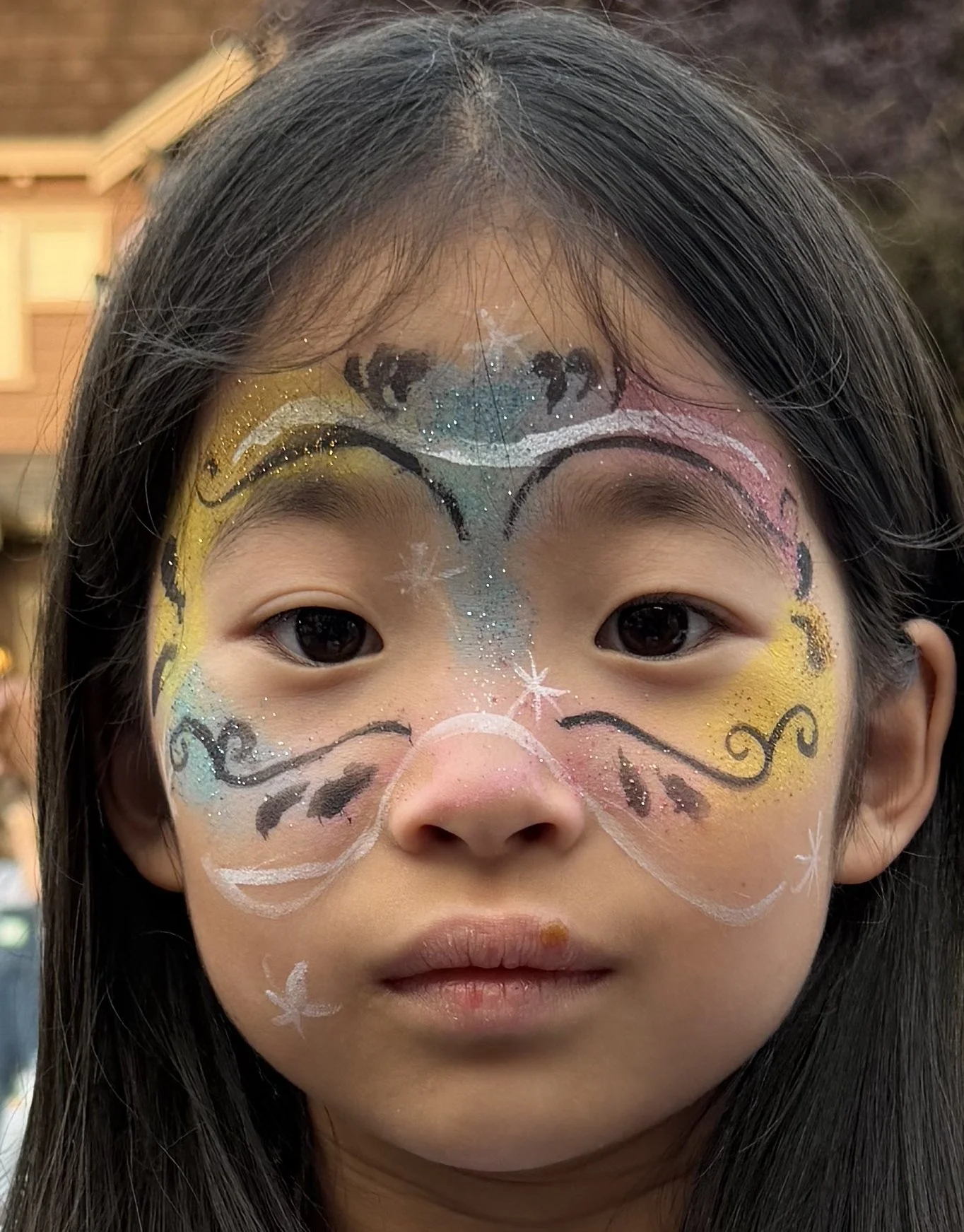 Close-up portrait of a child with colorful glitter face paint featuring a cat-inspired design