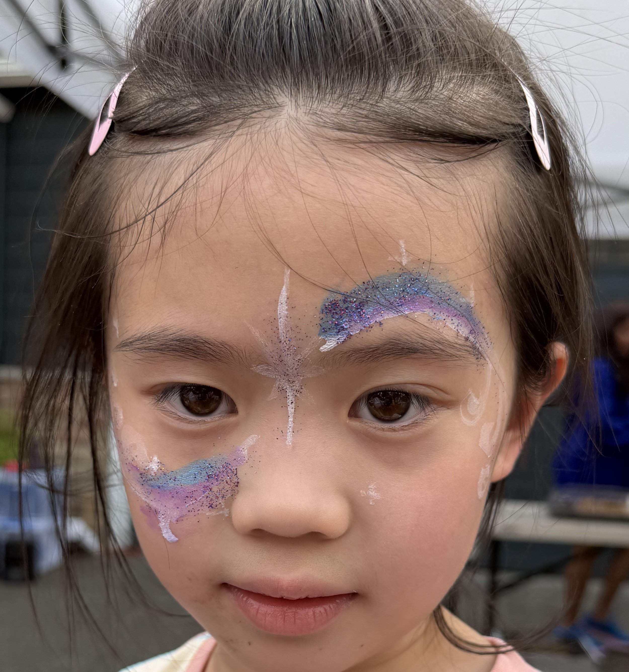Close-up of a young girl wearing glittery purple and blue face paint with pink hair clips
