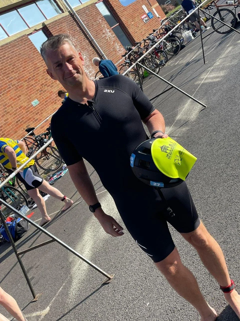 Man in black cycling gear holding a helmet at a bicycle race transition area