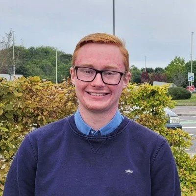 Smiling red-haired man wearing glasses and a navy sweater outdoors