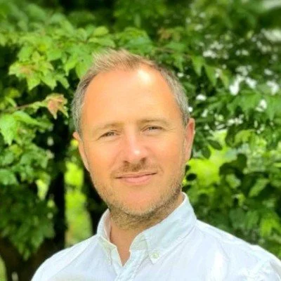 Portrait of a smiling middle-aged man in a white button-down shirt outdoors against green foliage