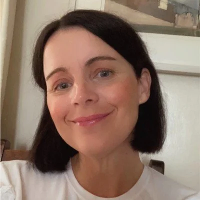 Close-up portrait of a smiling woman with dark shoulder-length hair wearing a white shirt indoors.