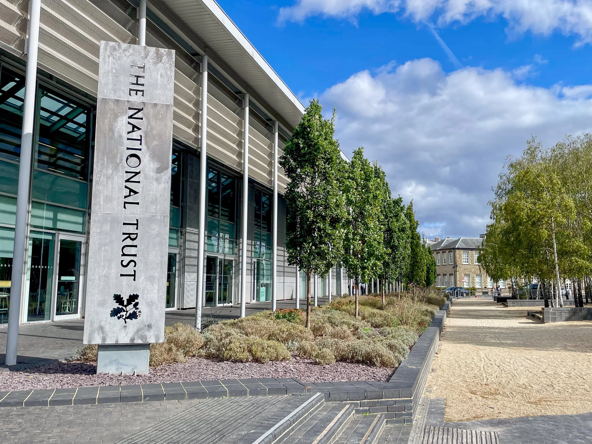 Exterior of the National Trust for Scotland building with landscaped courtyard, trees, and blue sky