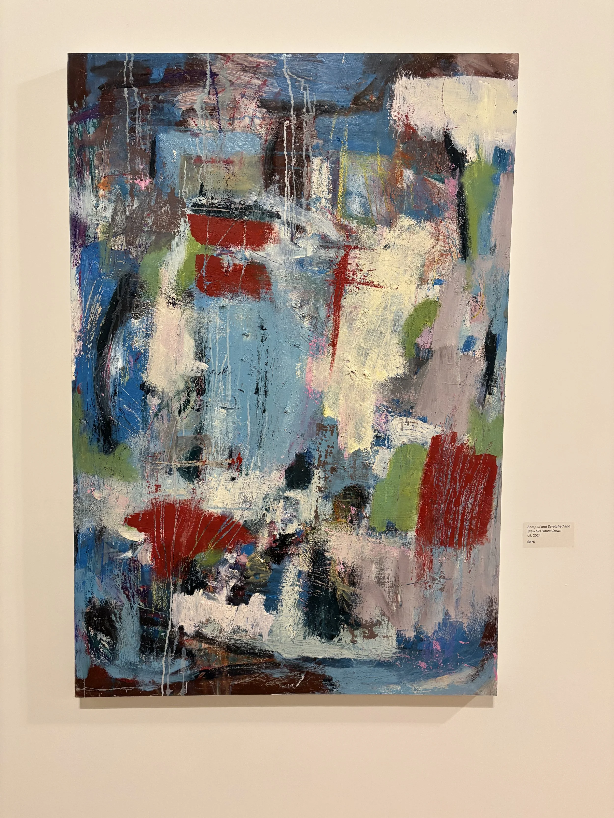 Large abstract mixed-media painting with layered blue, red, green, white, and black brushstrokes displayed in a gallery.