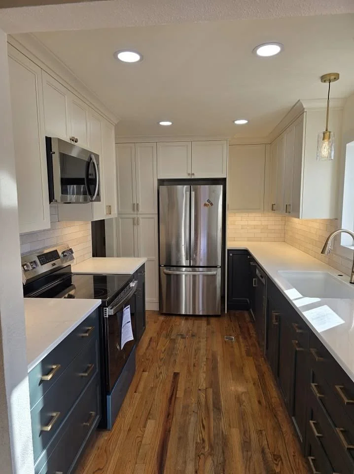 Modern galley kitchen with white cabinets, dark lower cabinets, stainless steel appliances, quartz countertops, subway tile backsplash, farmhouse sink, and hardwood floors
