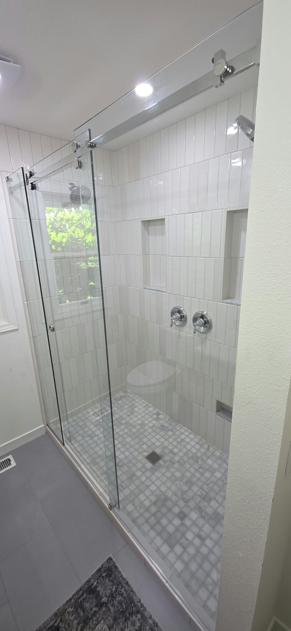 Modern walk-in shower with white subway tile walls, glass enclosure, rainfall showerhead, built-in niches, chrome fixtures, and mosaic tile floor
