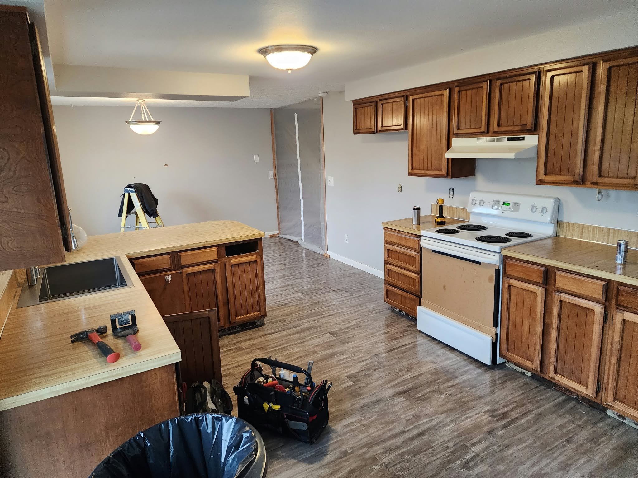 Kitchen renovation in progress with wood cabinets, laminate countertops, white electric stove, island, tools, and unfinished fixtures.