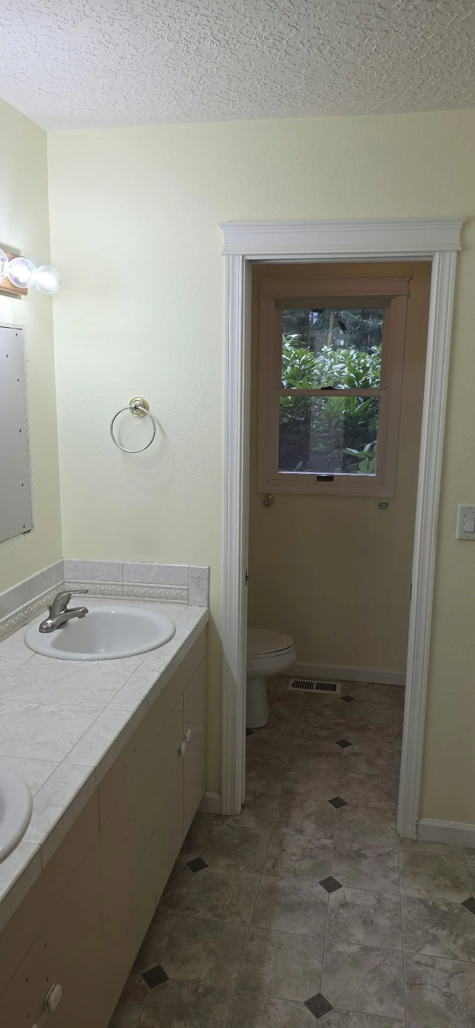 Bathroom vanity with tiled countertop, sink, towel ring, and doorway leading to a toilet room.