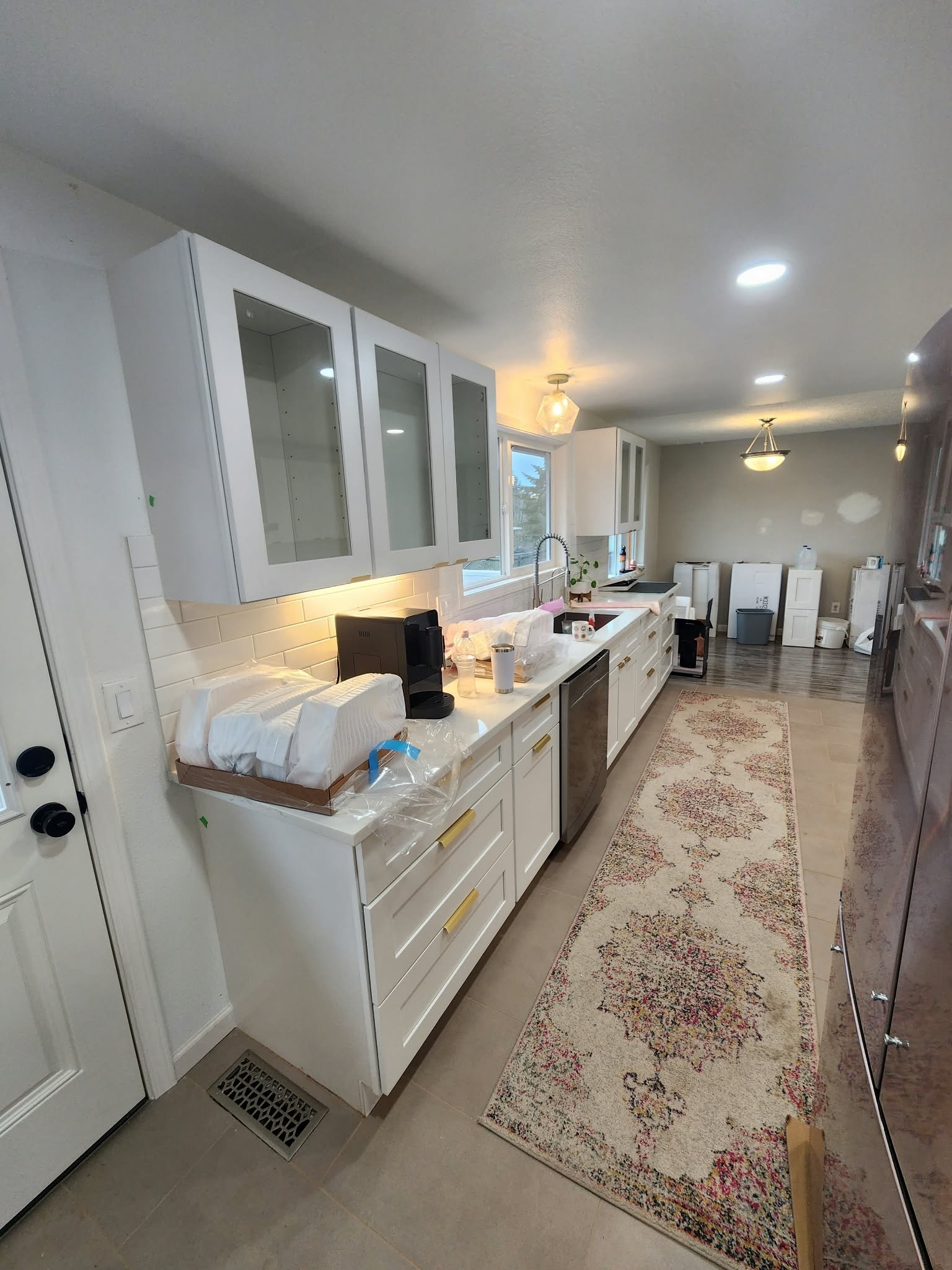 Bright modern galley kitchen with white cabinets, glass-front cupboards, island sink, stainless steel appliances, subway tile backsplash, and patterned runner rug