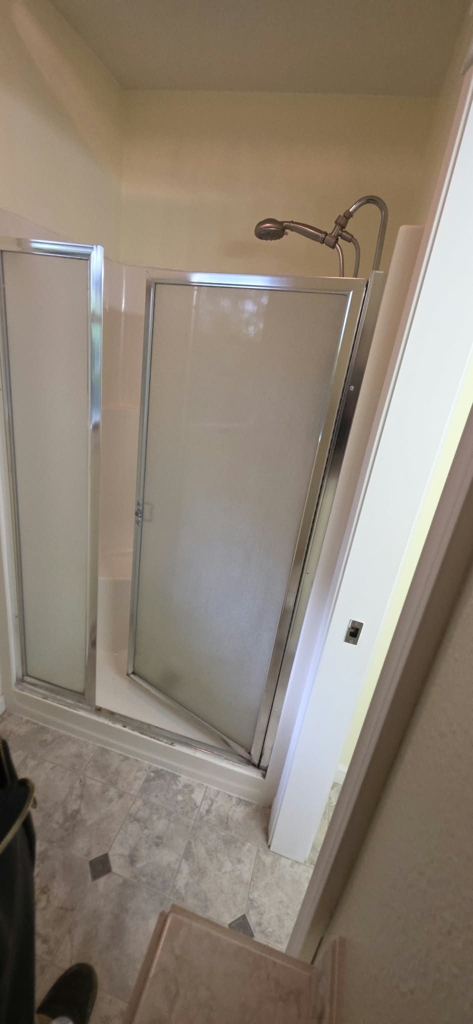 Bathroom shower stall with sliding frosted-glass doors, chrome trim, handheld showerhead, and tiled floor.