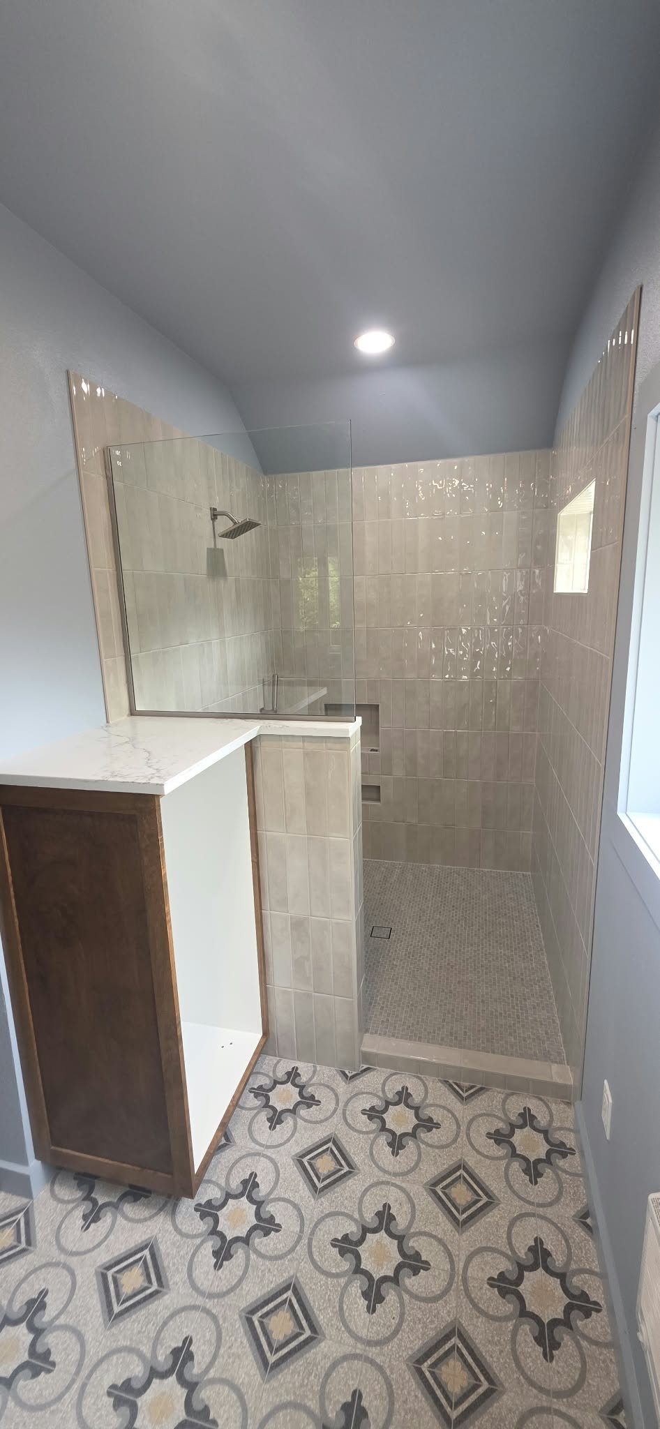 Modern bathroom with a tiled walk-in shower, glass partition, patterned tile floor, and wood vanity.