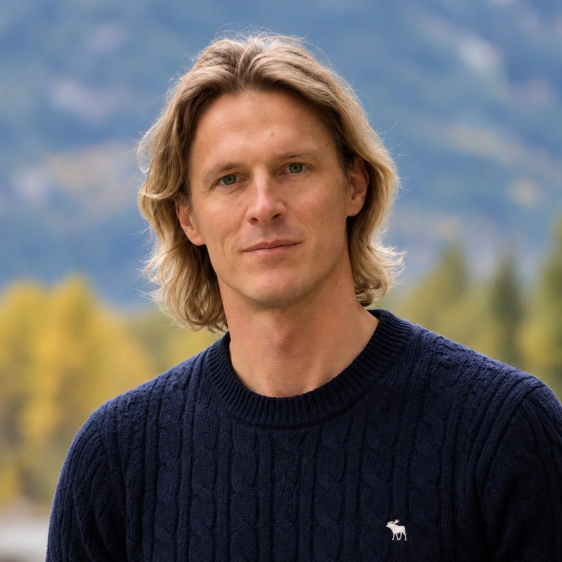 Portrait of a blond man wearing a navy cable-knit sweater outdoors